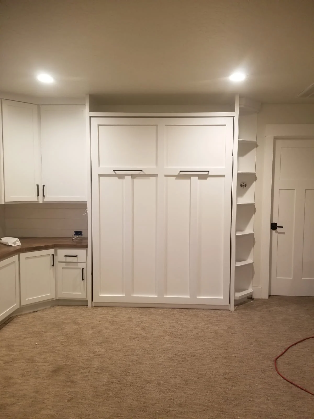 A built-in white cabinet with panel doors, located in a room with beige carpet and recessed ceiling lights.
