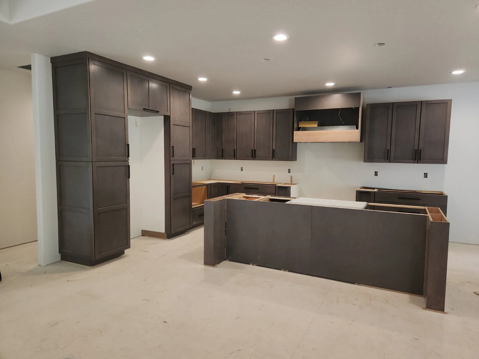 Kitchen cabinets being installed in a new kitchen, with some upper and lower cabinets, but without countertops yet.