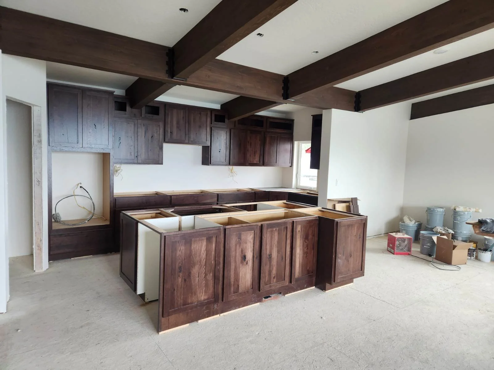 Kitchen under construction with dark wooden cabinets, a centered kitchen island with open cabinetry, and construction supplies and tools on the floor.