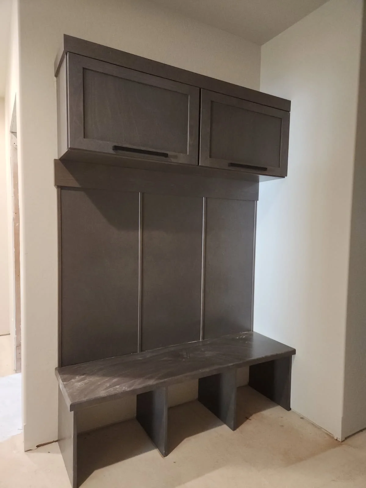 A gray wooden hallway bench with open storage compartments underneath and a matching wall-mounted cabinet above, set against a plain wall.