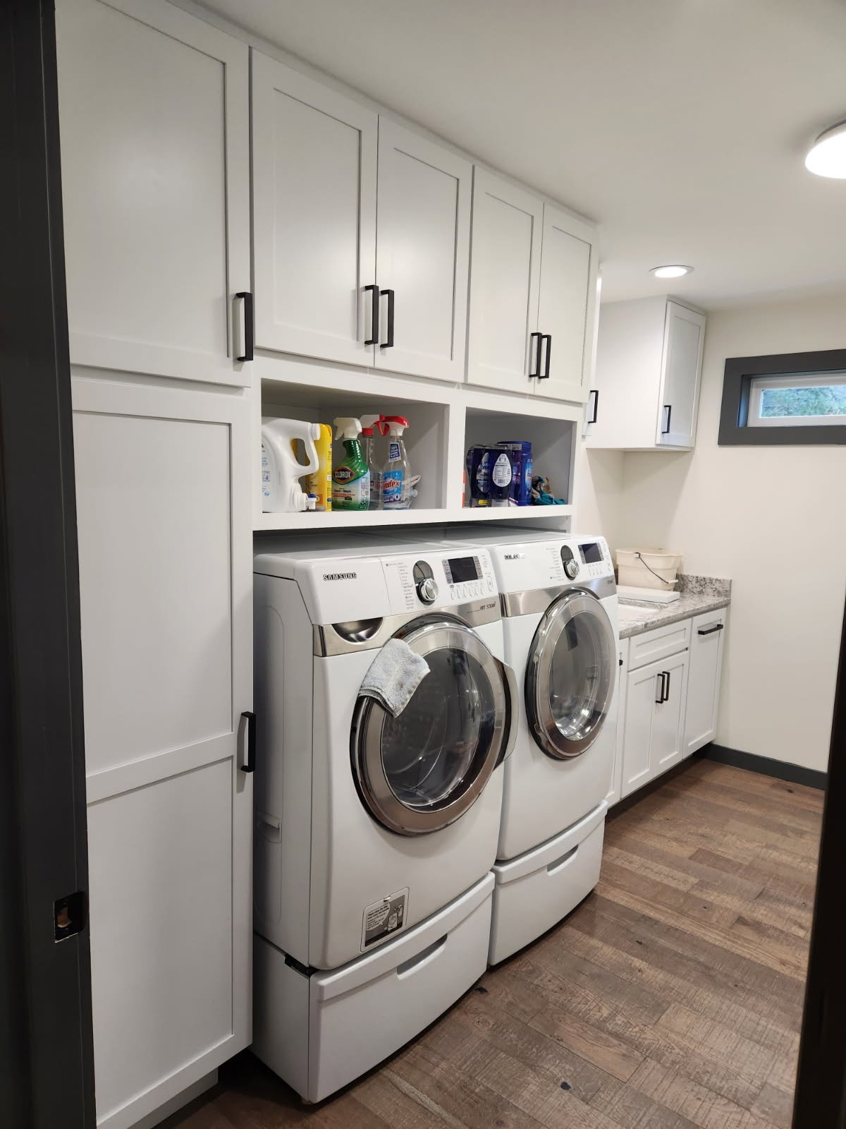 Coeur d'Alene Laundry room with white cabinets, a washer and dryer, laundry supplies in open shelves, and a window.