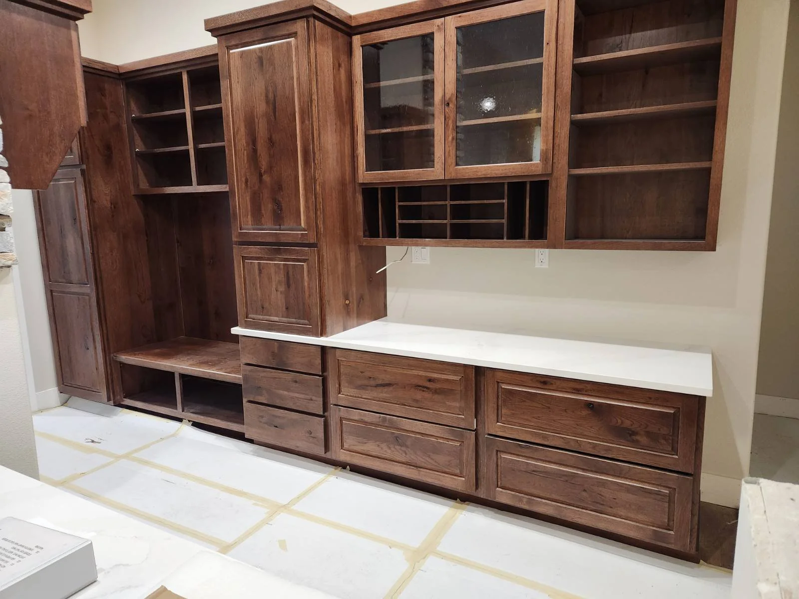 Wooden kitchen cabinets with glass doors and open shelves, white countertop, and empty wall space.