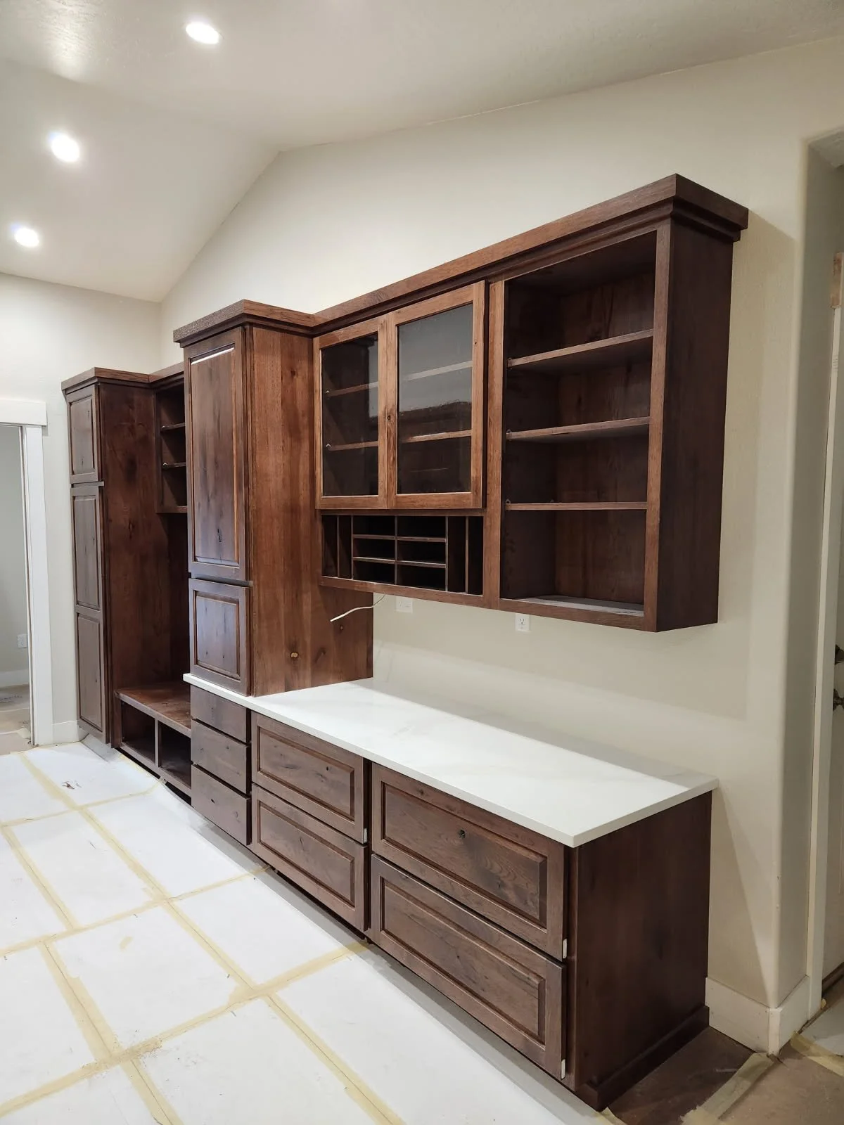 Wooden kitchen cabinets with glass and open shelving, white countertop, in a kitchen under construction.