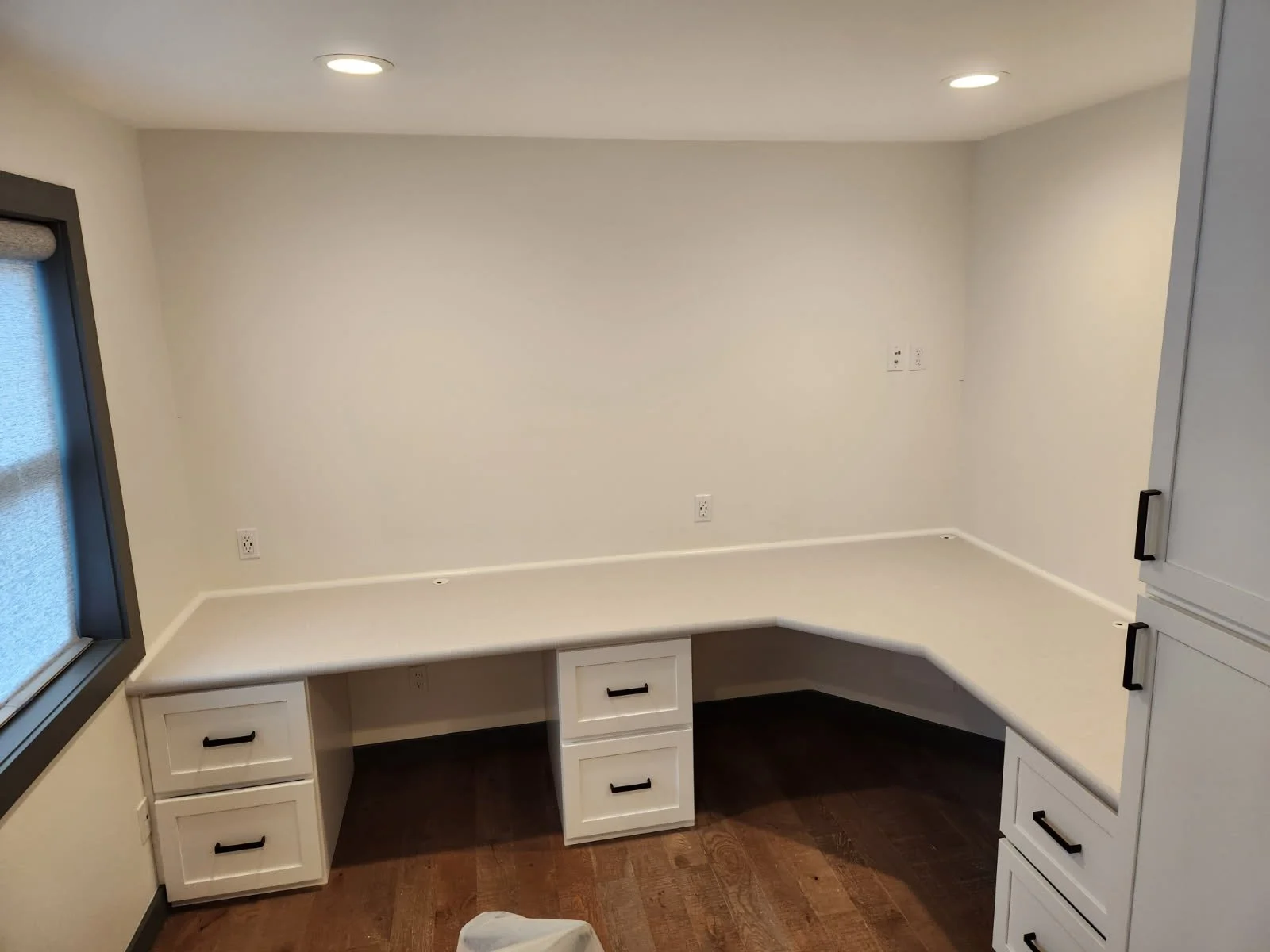 Empty home office or kitchen corner with white cabinetry, built-in desk, and hardwood floors.