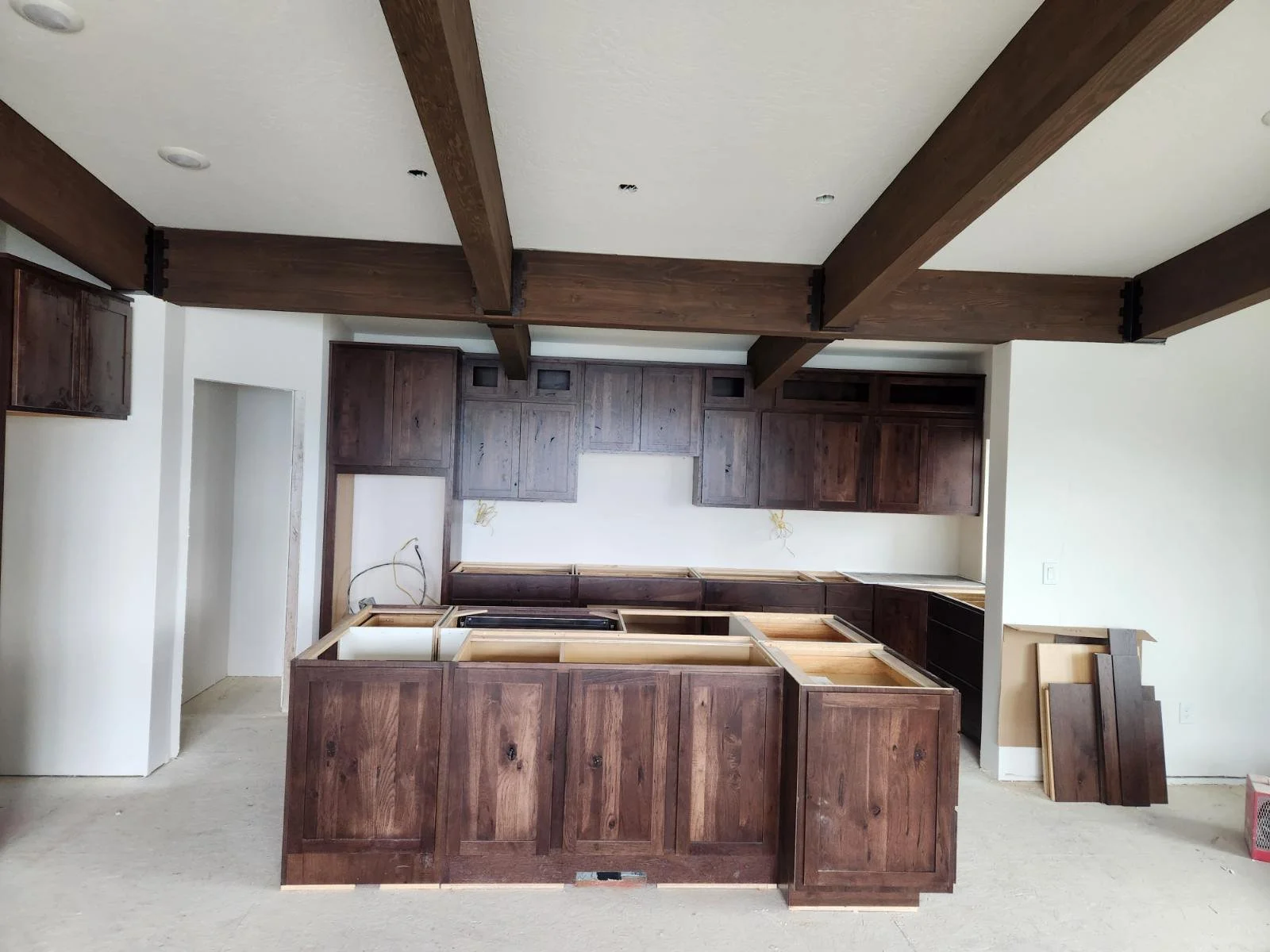 Kitchen under construction with dark wood cabinets and ceiling beams, and an unfinished island with open frame.