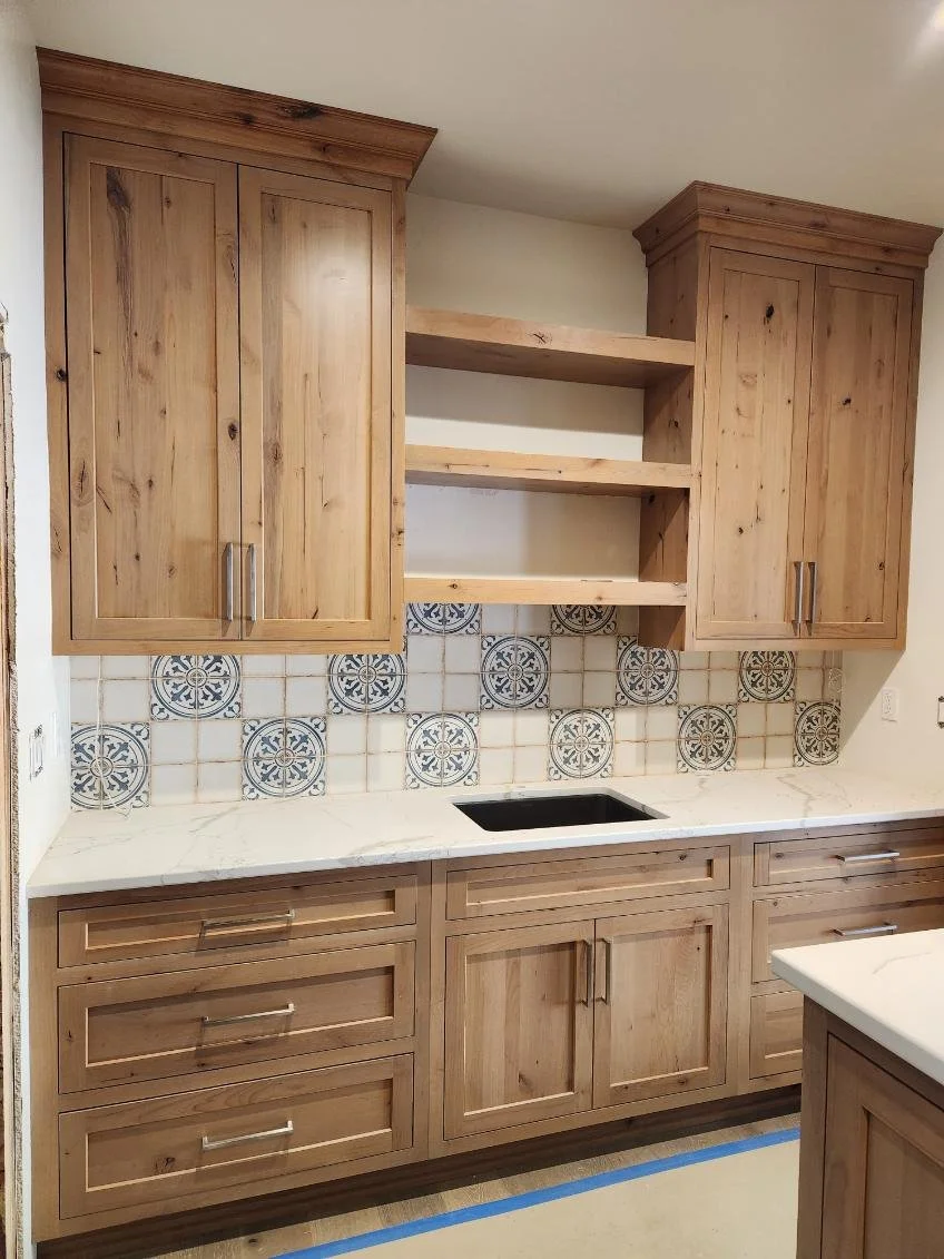 Kitchen with wooden cabinets, open shelves, a marble countertop, and a black sink hole, with patterned tile backsplash.