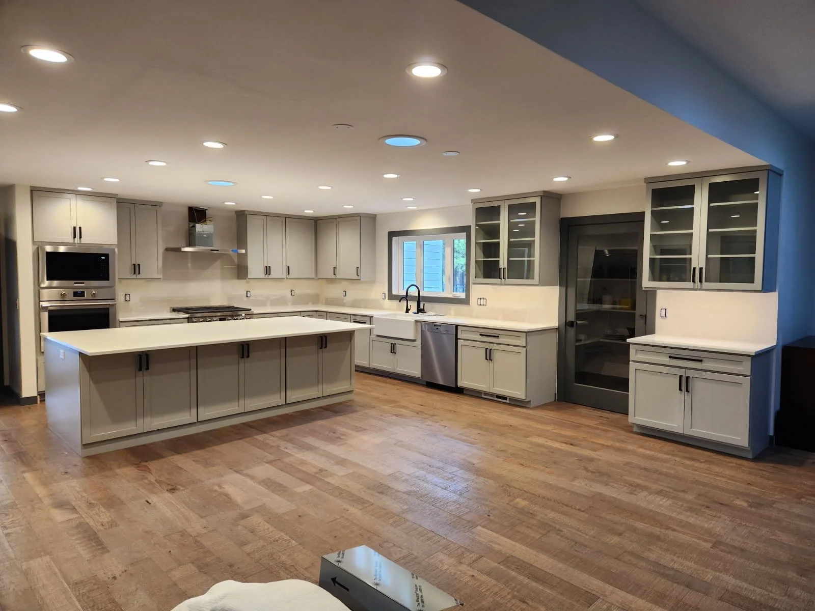 Coeur d'Alene Modern kitchen with white cabinets, a large island, stainless steel appliances, and a wooden floor.