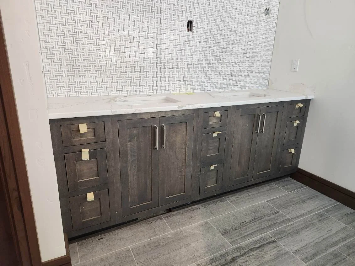 Kitchen cabinet with dark wood finish, white marble countertop, and a decorative tiled backsplash in a herringbone pattern. The cabinet has multiple drawers and doors with metal handles, and are covered with painter's tape.