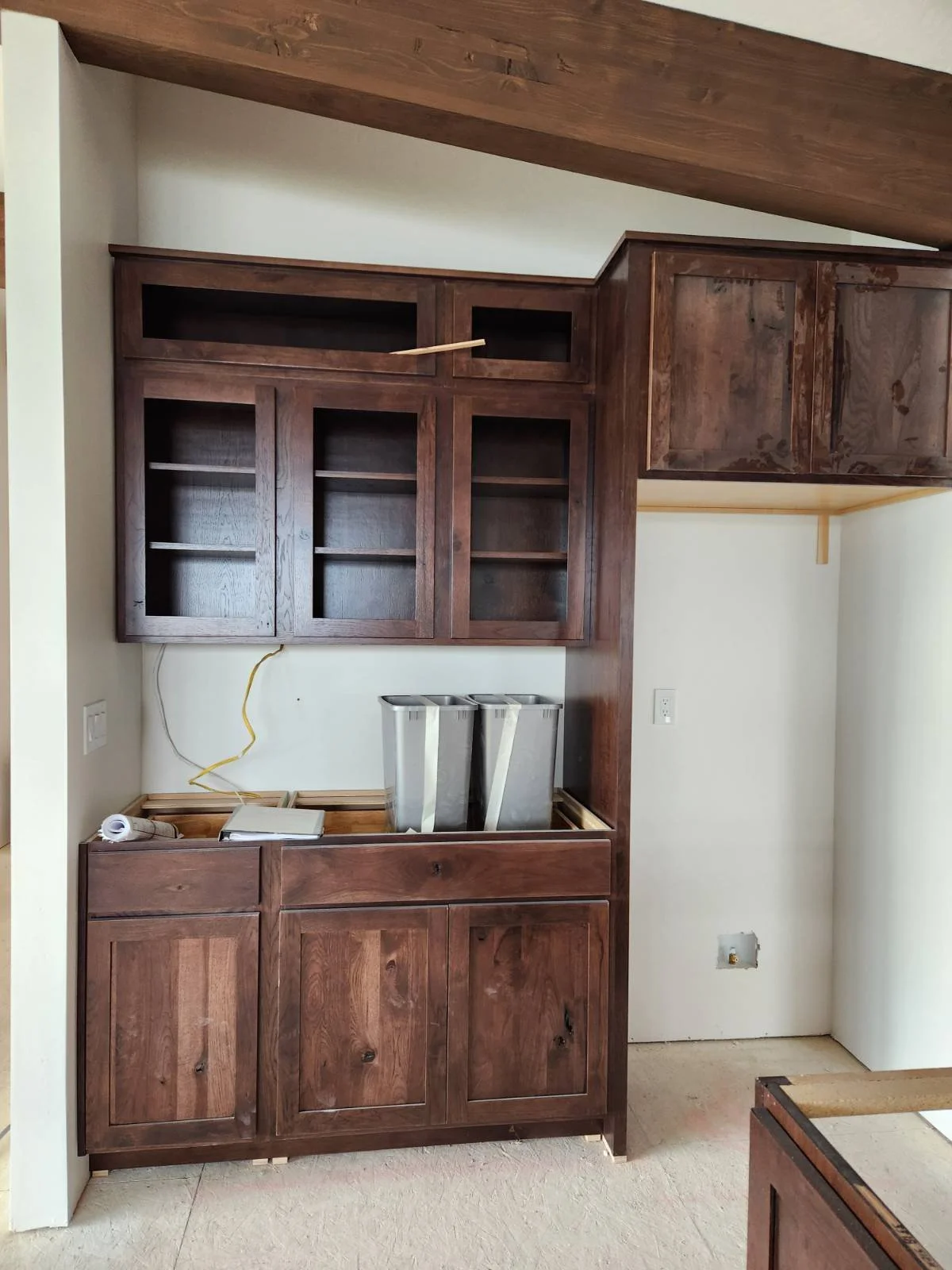Undeveloped kitchen cabinetry with upper glass doors, lower cabinets, and countertops, with some construction tools and materials visible.