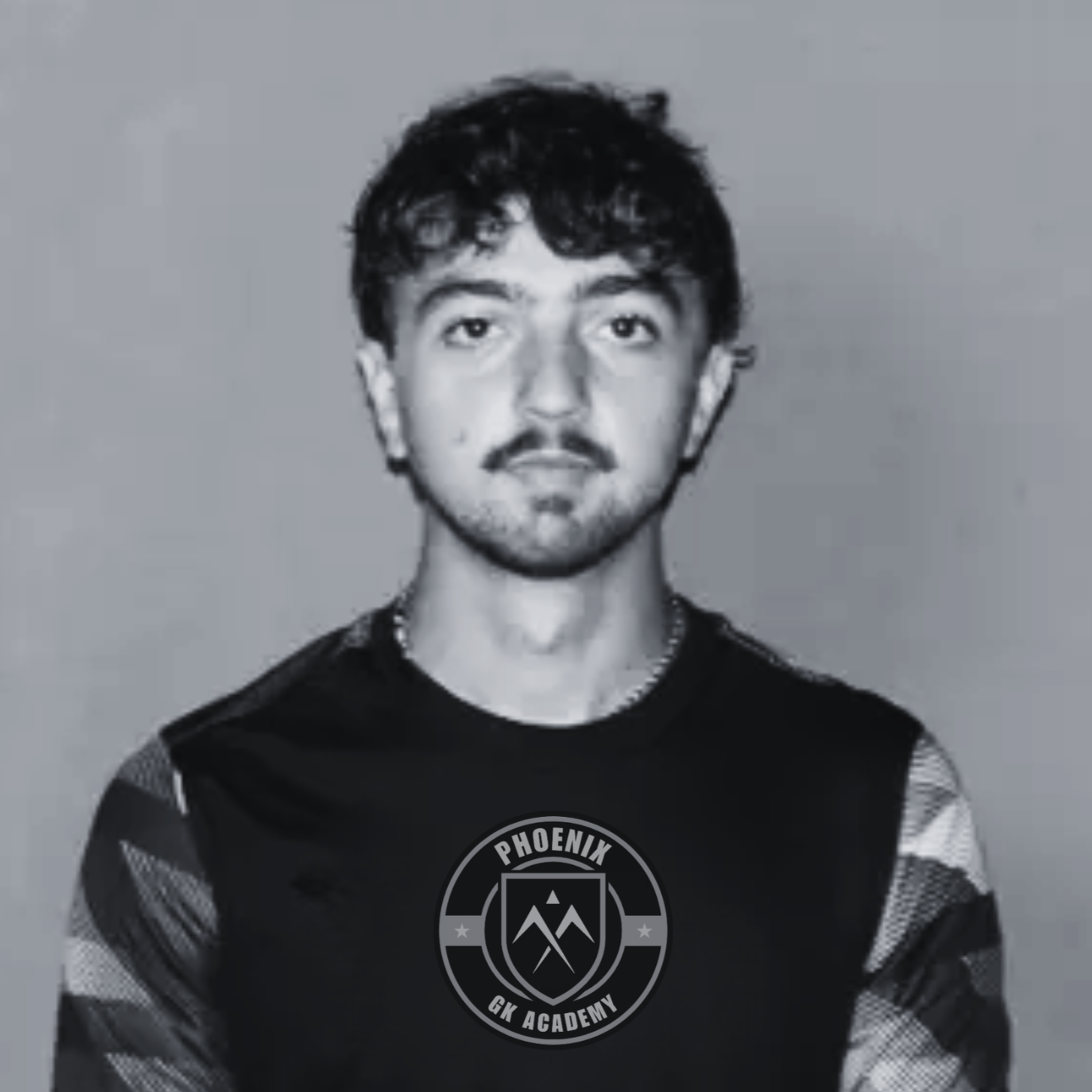A young man with short dark hair, wearing a black sleeveless shirt with a logo that reads "Phoenix GK Academy" on the front, standing against a plain background.