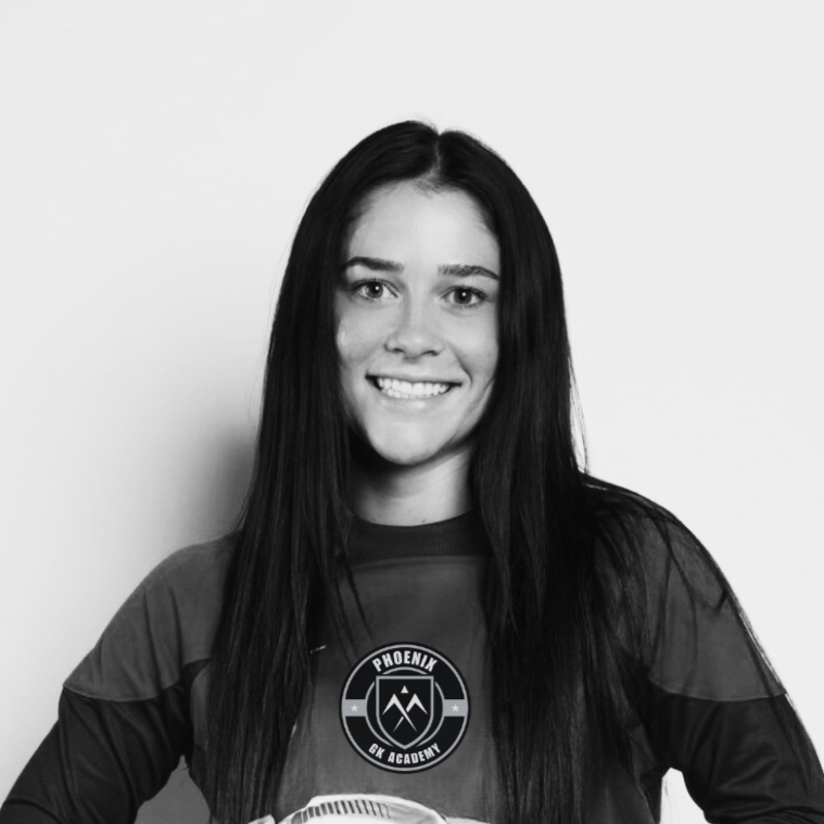 Black and white photo of a young woman with long dark hair, smiling, wearing a sports jersey with a logo that says Phoenix GK Academy, standing against a plain light-colored background.