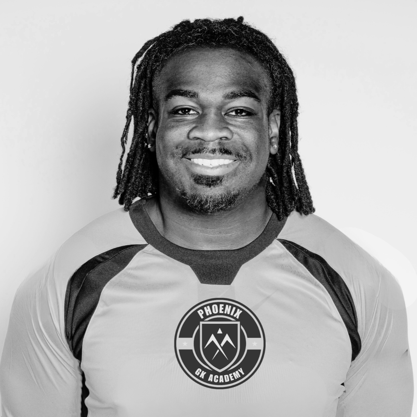 Black and white photo of a man smiling, wearing a sports jersey with the logo "Phoenix GK Academy" on the chest.