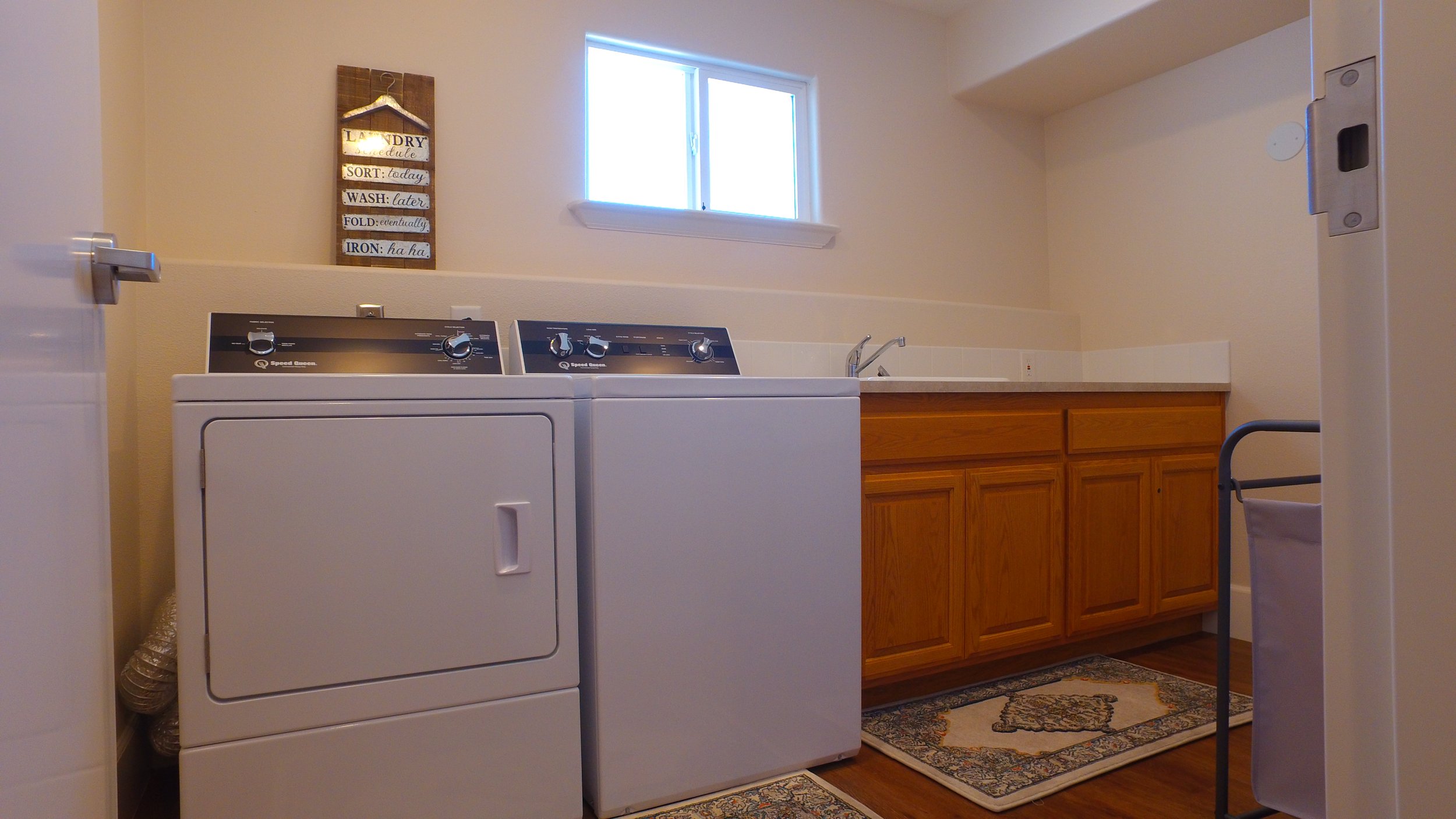Laundry room with a washer, dryer, wooden cabinets, a window, a wall sign, and a cart.
