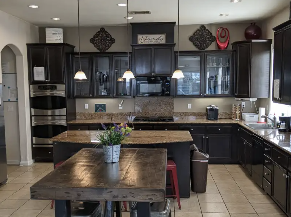 Kitchen with dark cabinets, granite countertops, a center island with a flower pot, and pendant lights.