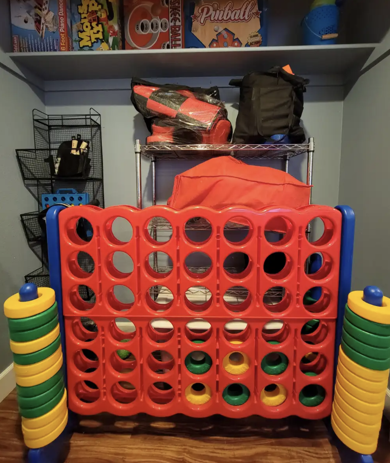 Colorful oversized Connect Four game set in a room with board games on the shelf above.