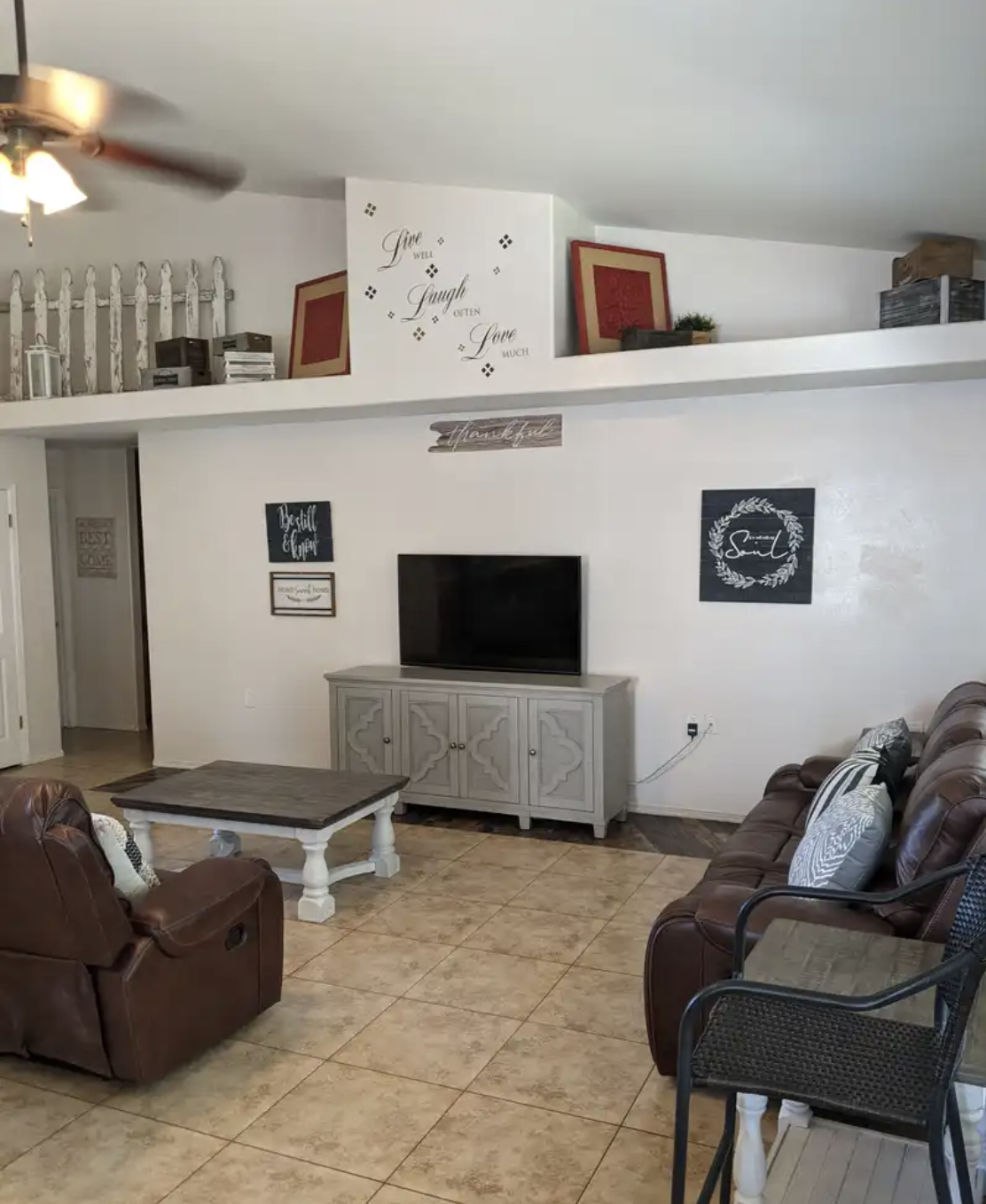 Living room with two brown leather sofas, a gray cabinet with television, wall decor, and a tile floor.
