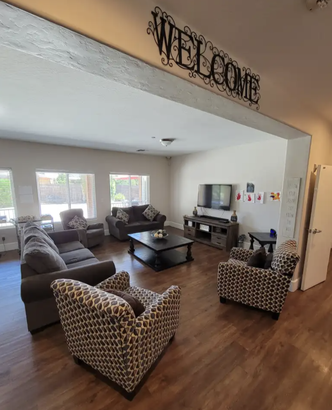 Living room with three sofas, two patterned armchairs, a TV on a stand, and a wooden coffee table, with windows letting in natural light.