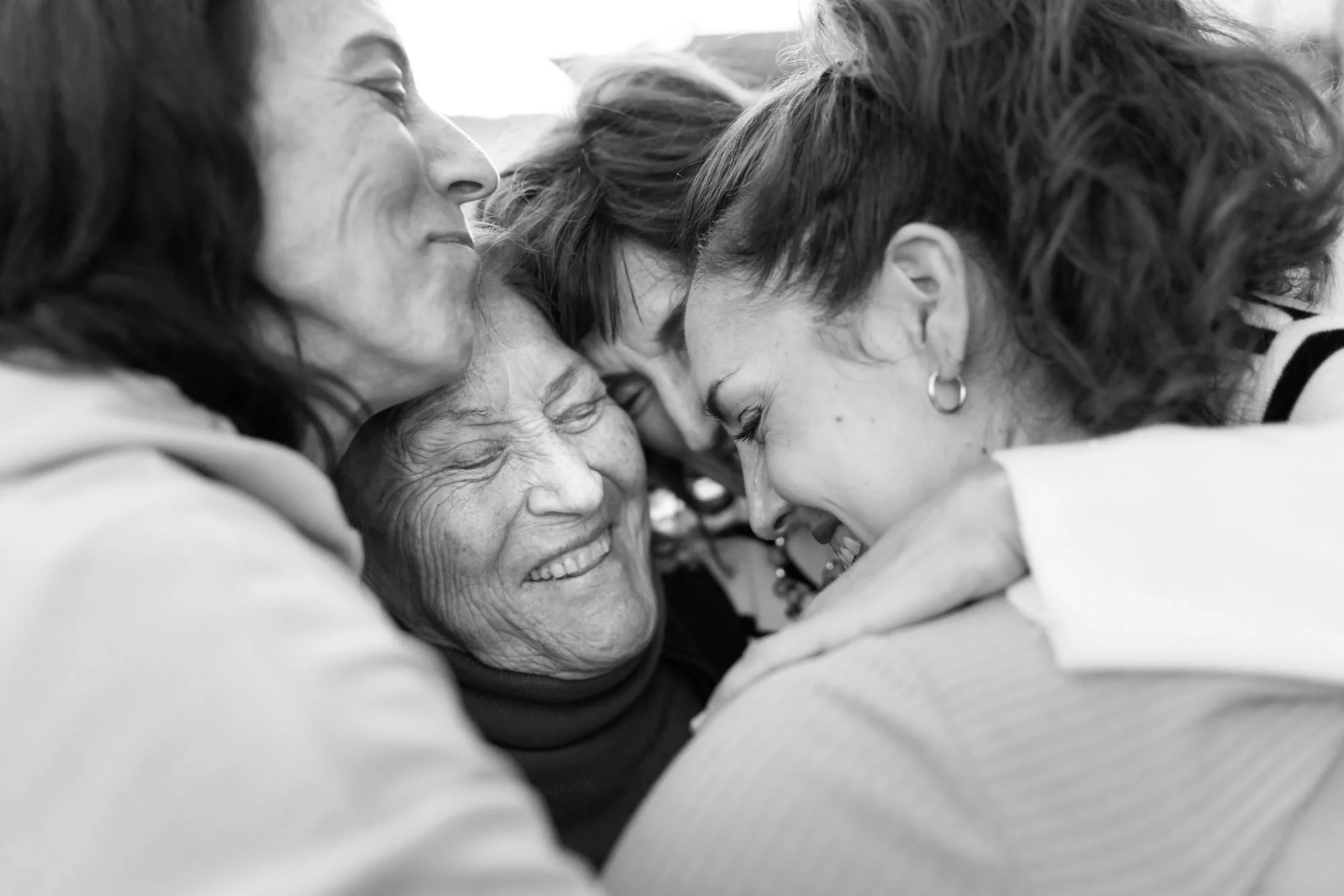 Four women sharing a close, joyful group hug, smiling and embracing each other.