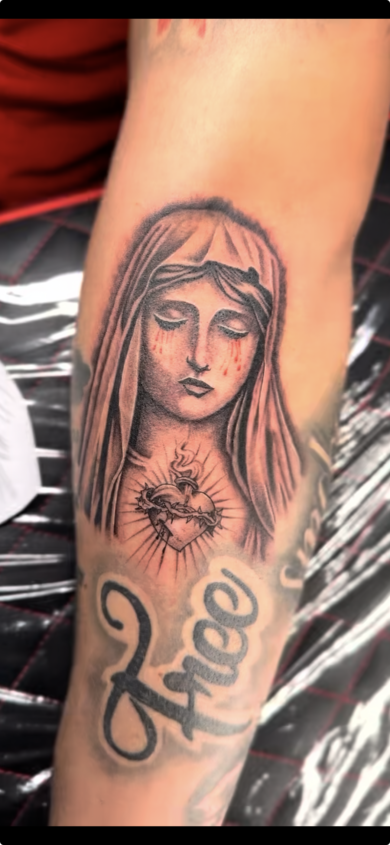 Tattoo of a woman's face with tears and a heart with a crown of thorns and a small flame, along with the word 'faith' below.