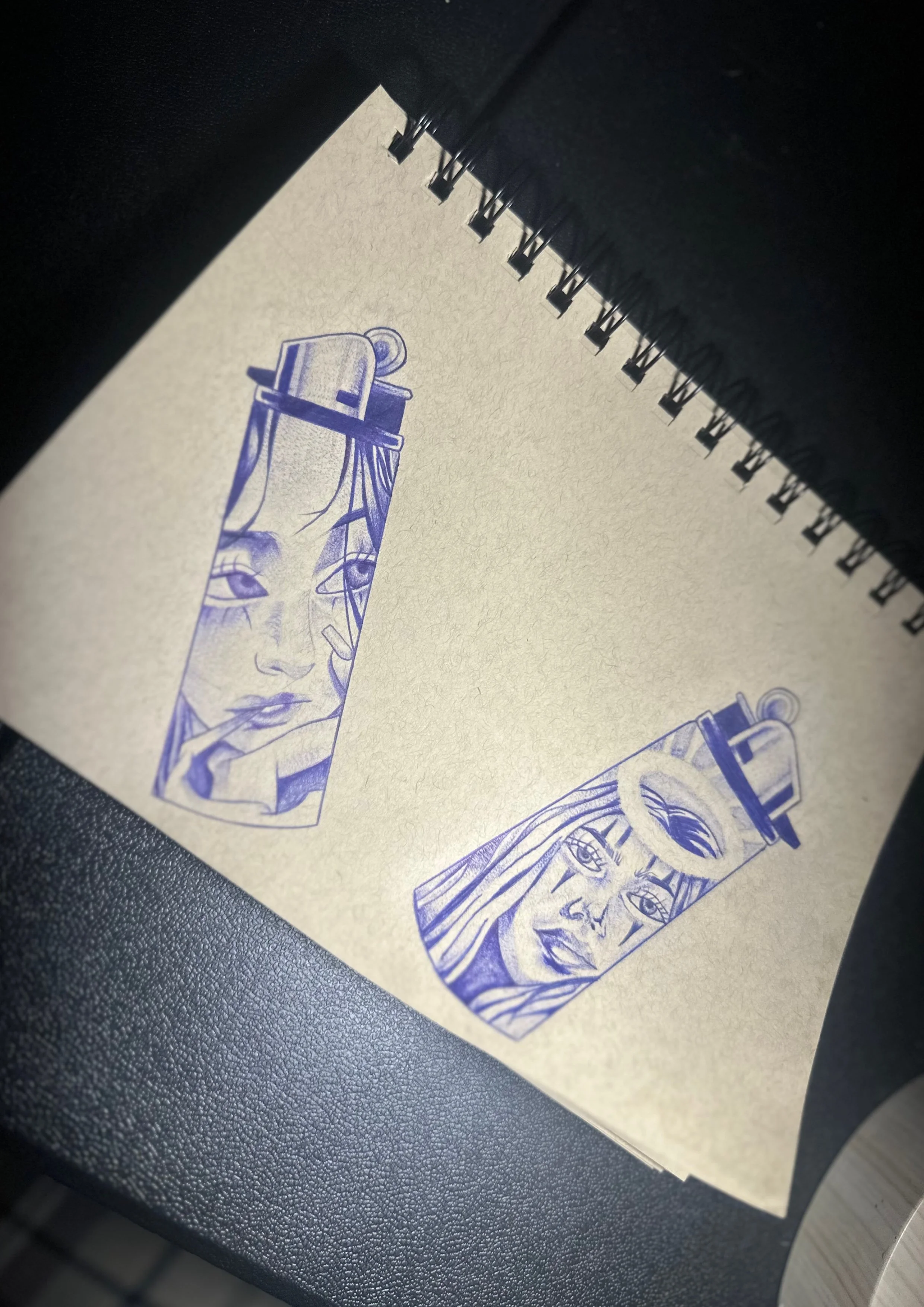 Sketches of two spray paint cans with female faces drawn in blue ink on the cans, depicting detailed and expressive features.