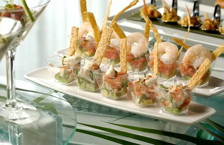 Individual shrimp cocktail appetizers with diced vegetables, topped with crispy breadsticks in clear cups