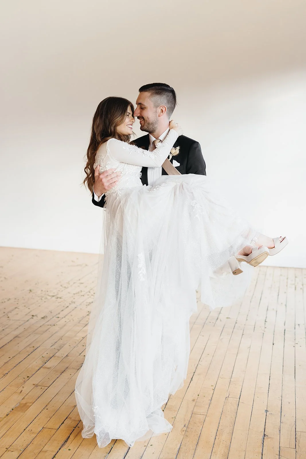 A bride in a white wedding dress and a groom in a black tuxedo holding each other in a dance pose.