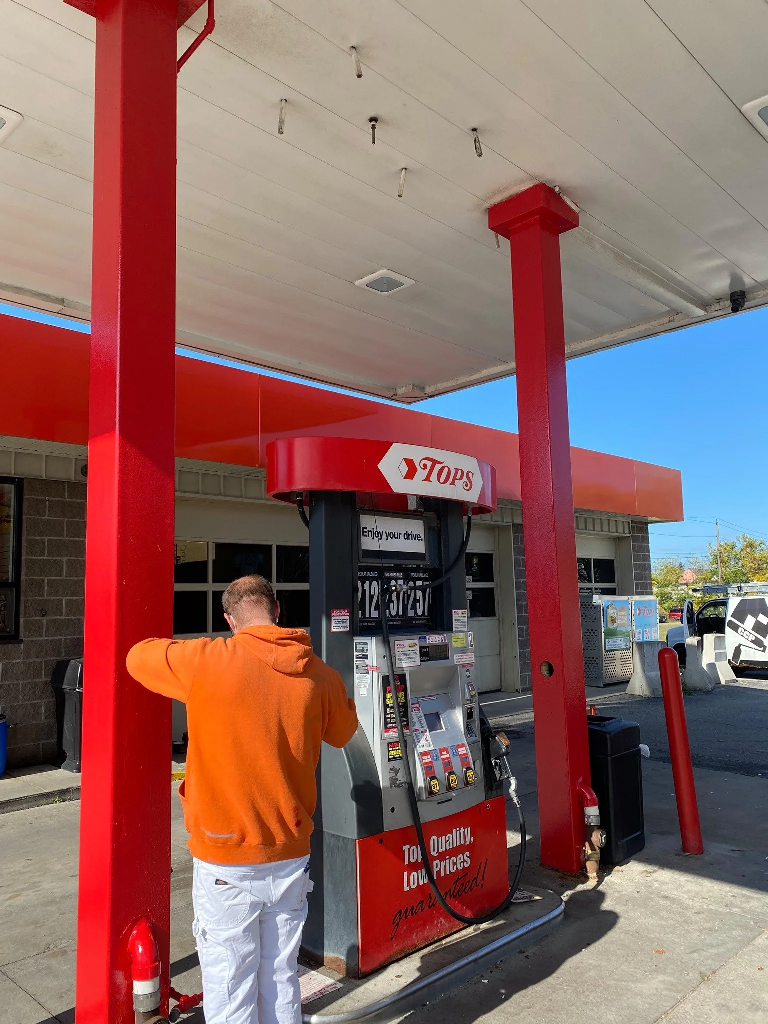 Person in orange hoodie filling up gas at a gas station with a red and black fuel pump.