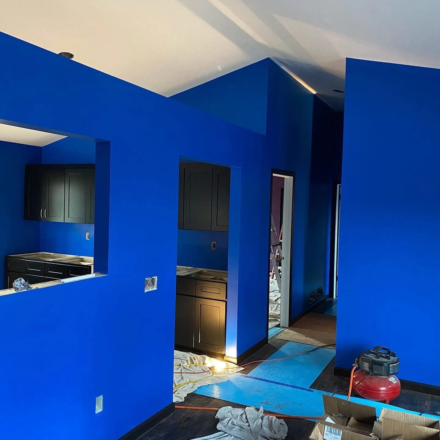 Interior of a room under renovation with bright blue walls, black cabinets, and construction tools on the floor.