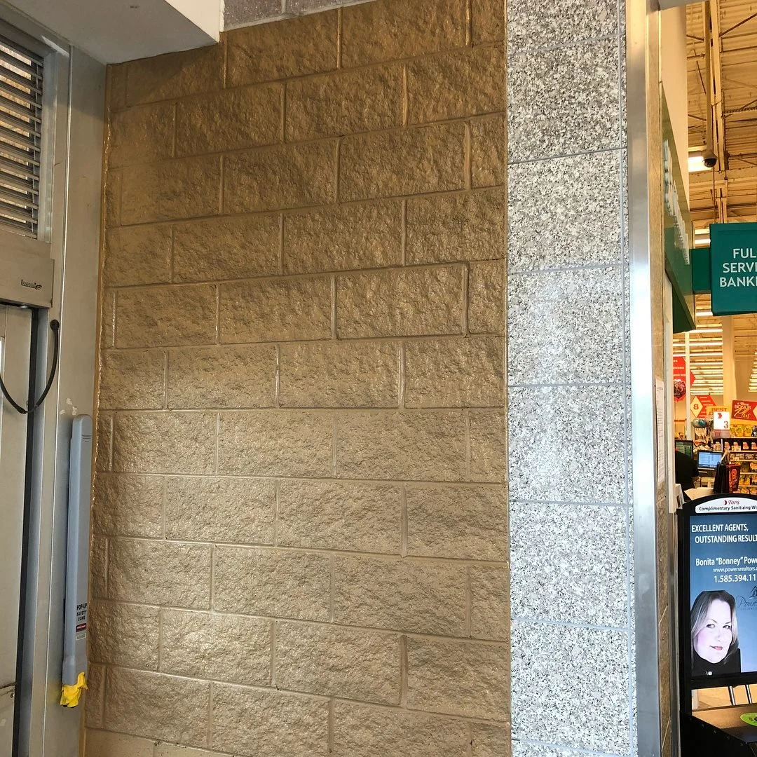 Image showing a section of a wall with beige and gray bricks, with a visible ATM machine and a digital display in the background in a retail store.