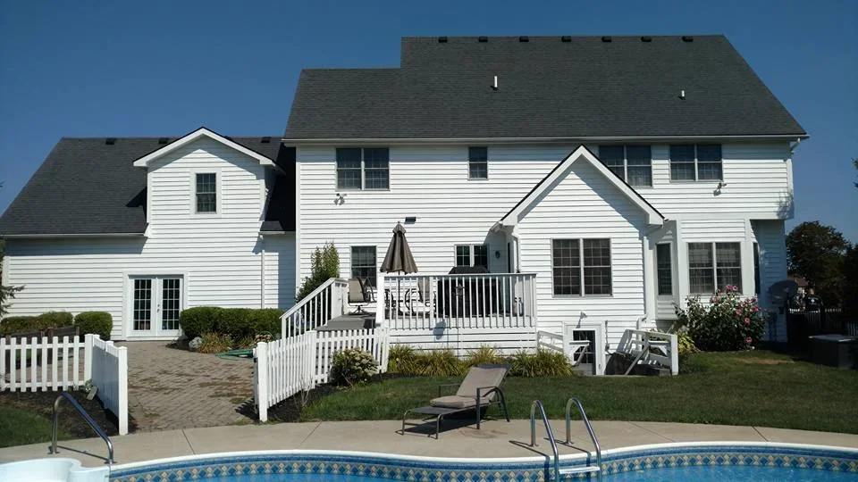 White two-story house with a backyard patio, lawn chairs, and swimming pool.
