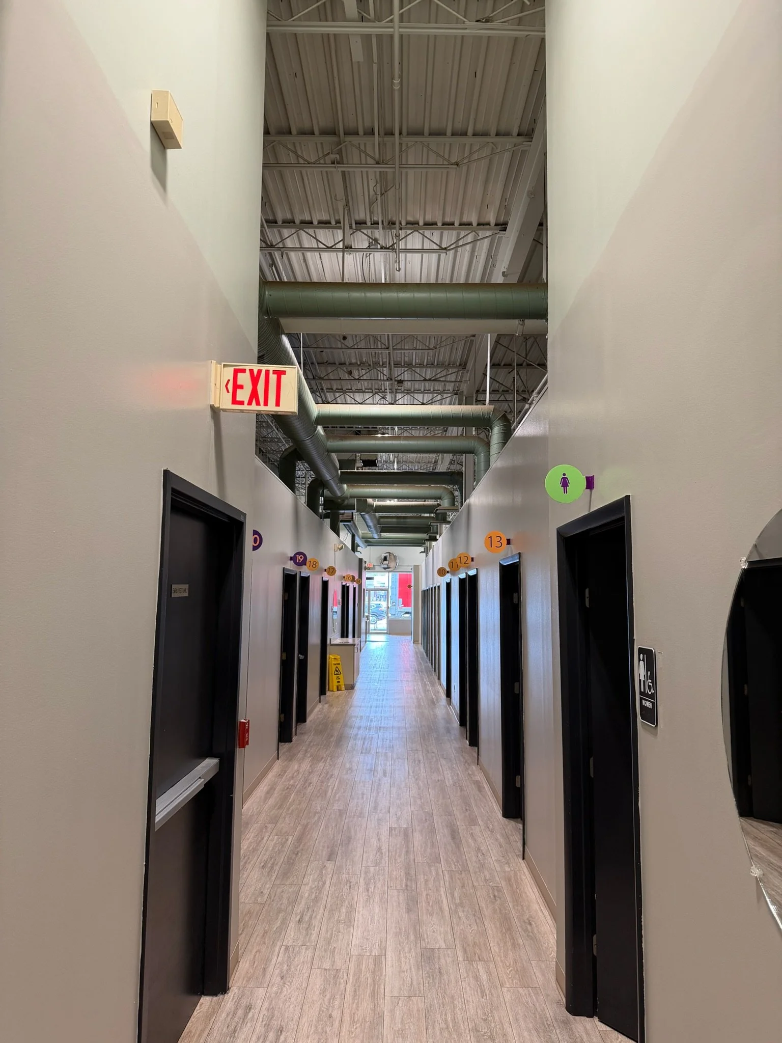 Indoor hallway with multiple restroom doors, colorful signs, and a view of the street outside.