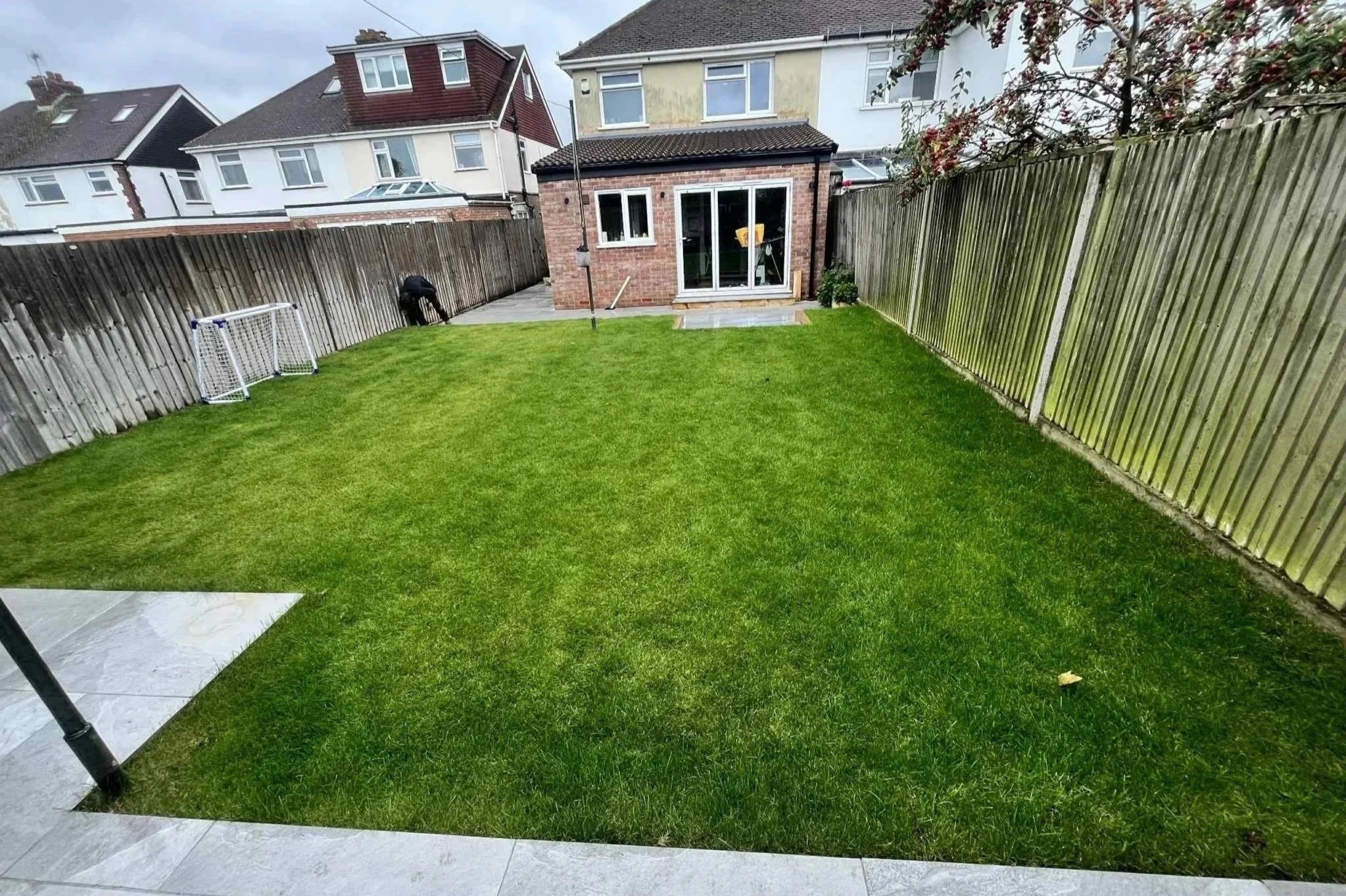 View of a backyard with a green lawn, wooden fence, small soccer goals, and a garden room at the back of the yard.