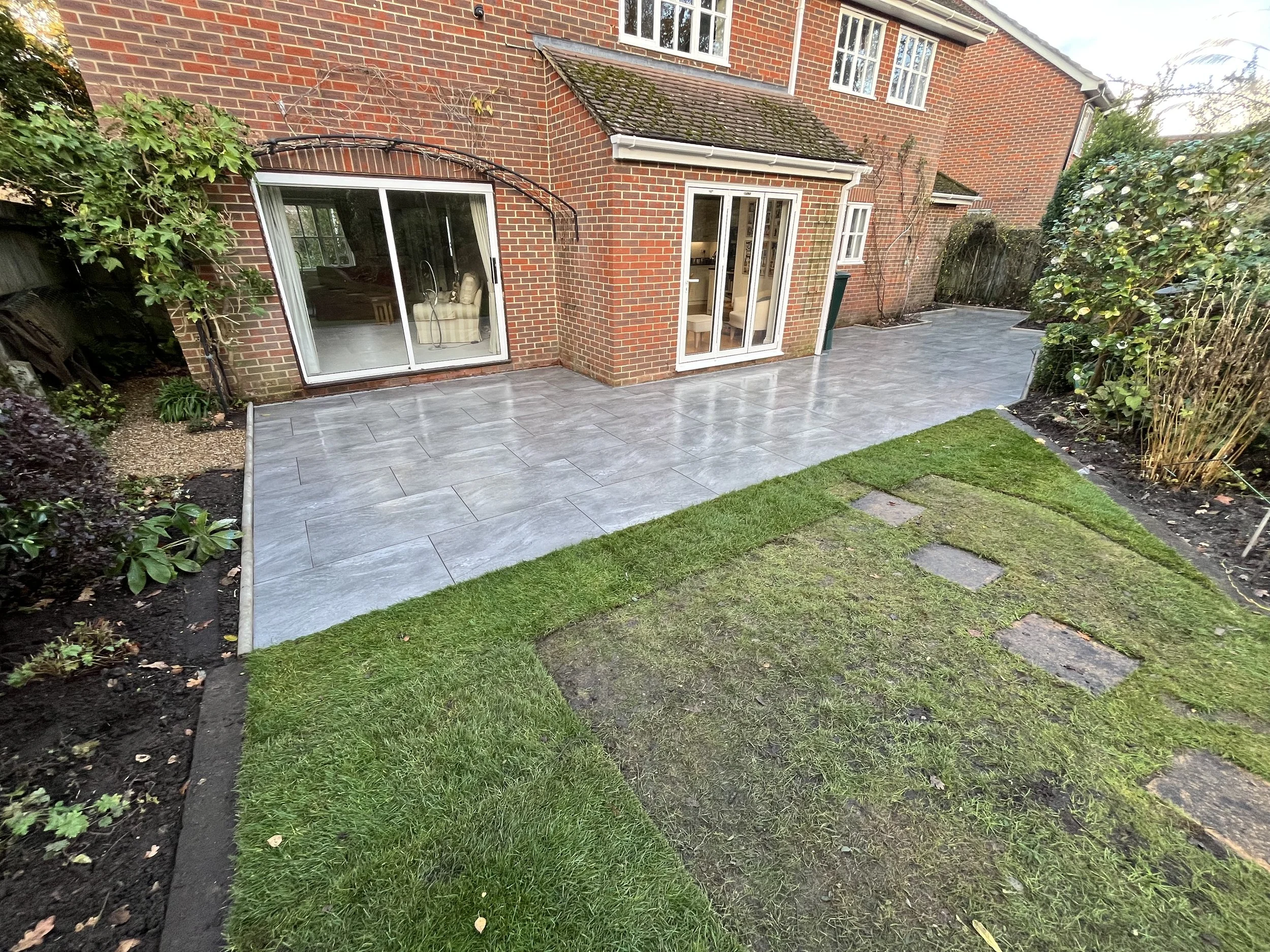 Backyard with new gray tiled patio and a small grassy area with stepping stones.