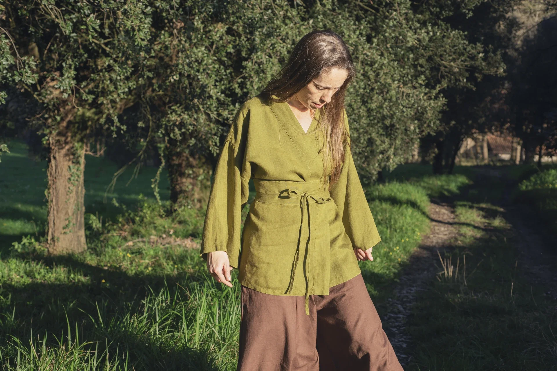 Mujer en la naturaleza vistiendo un kimono corto cruzado de lino color verde oliva, confeccionado de forma artesanal con tintes naturales libres de tóxicos.