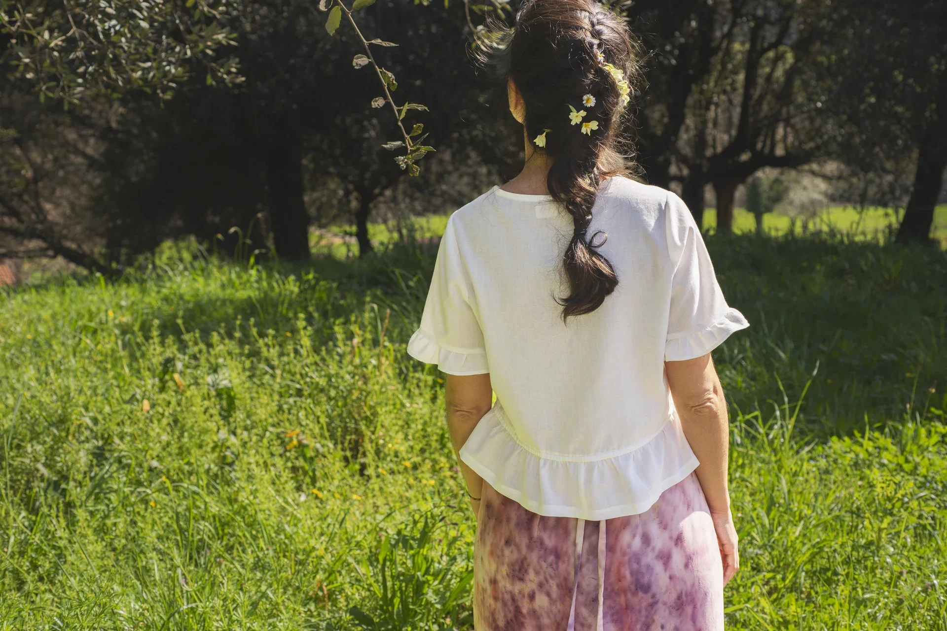 Blusa Aura de algodón orgánico en blanco, destacando sus botones de madera en forma de flor y el lazo ajustable en la cintura.