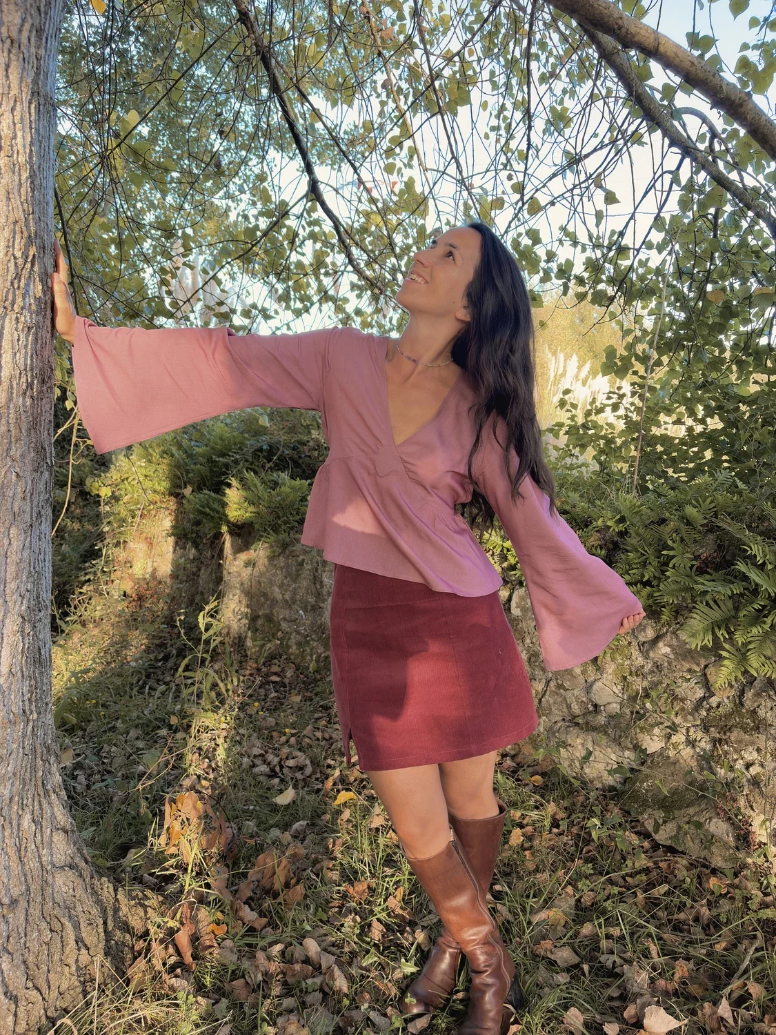 Mujer en la naturaleza luciendo la blusa mística Devi en color violeta, destacando las amplias mangas acampanadas y el tejido teñido con plantas medicinales