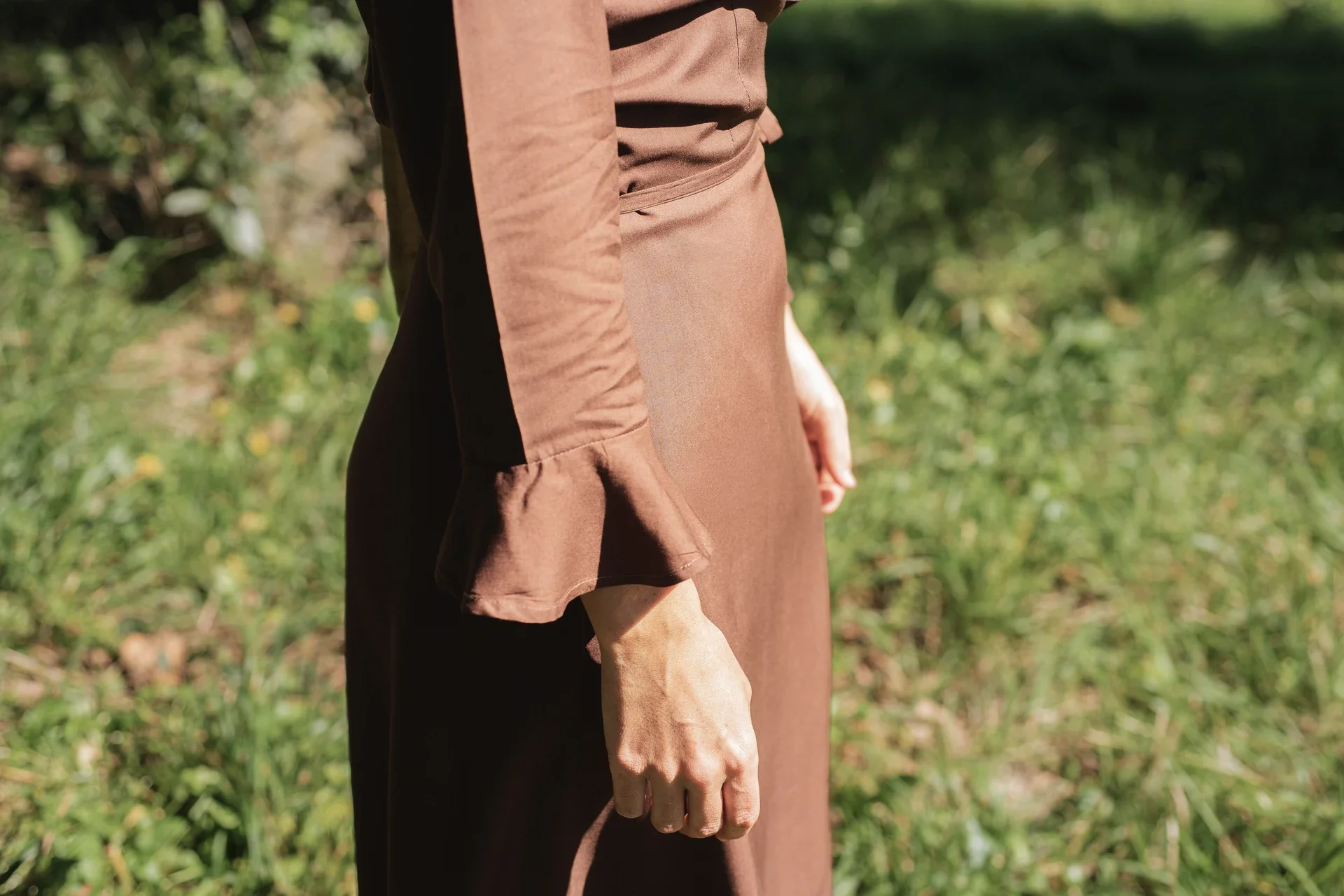 Mujer paseando por el campo vistiendo el vestido cruzado Agni en color marrón. Confeccionado en fibra de loto, alternativa vegana a la seda, y teñido con piel de granada y catechu