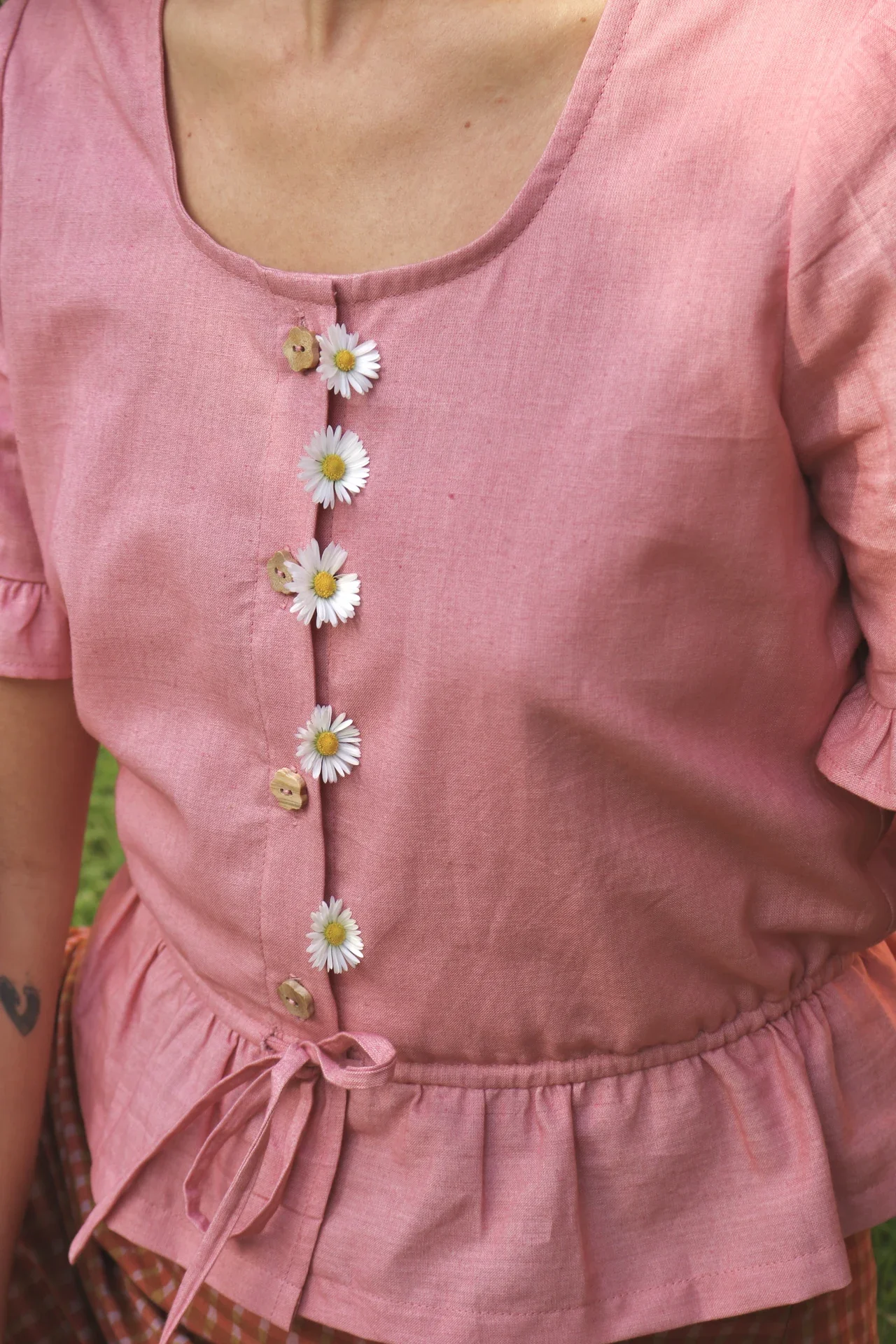 Blusa Aura de algodón orgánico en rosa de Madder Root, destacando sus botones de madera en forma de flor y el lazo ajustable en la cintura.