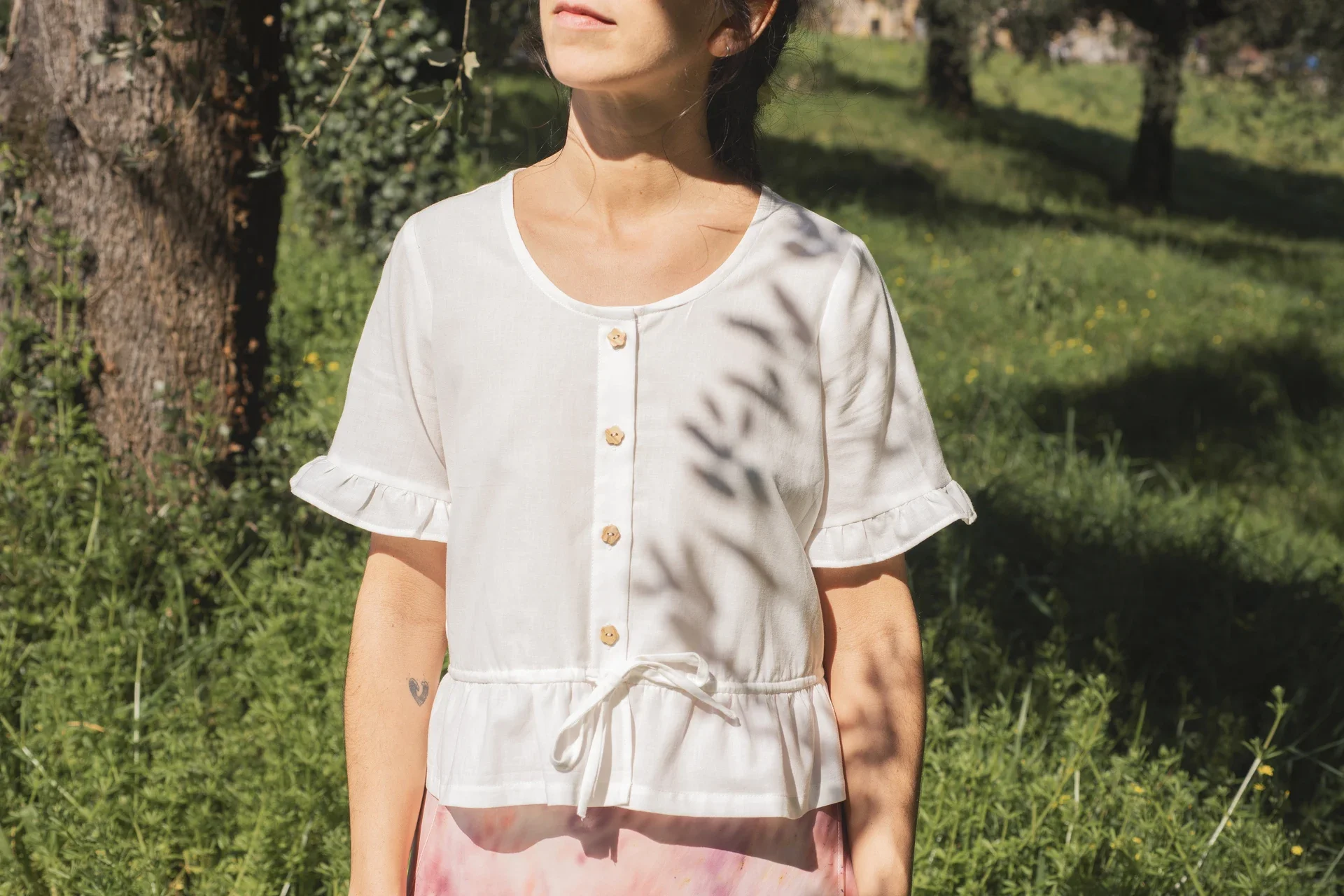 Blusa Aura de algodón orgánico en blanco, destacando sus botones de madera en forma de flor y el lazo ajustable en la cintura.