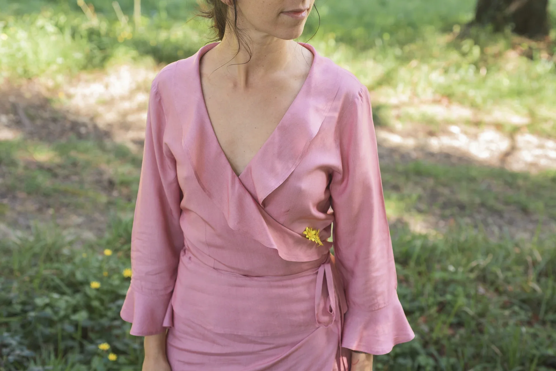 Mujer vistiendo la Blusa Agni cruzada de color rosa suave, confeccionada en fibra de loto natural con detalles de volantes en las mangas