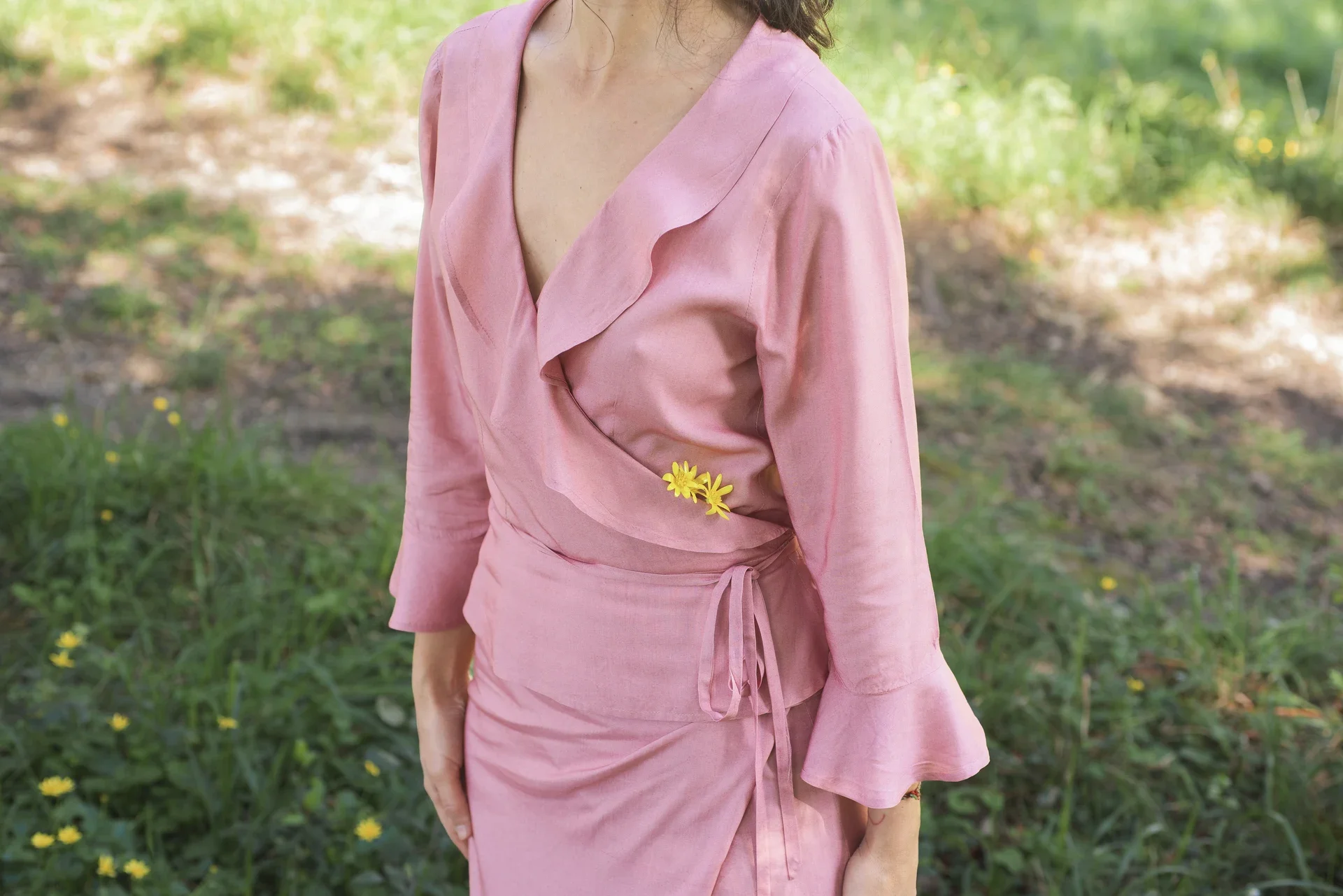 Mujer vistiendo la Blusa Agni cruzada de color rosa suave, confeccionada en fibra de loto natural con detalles de volantes en las mangas