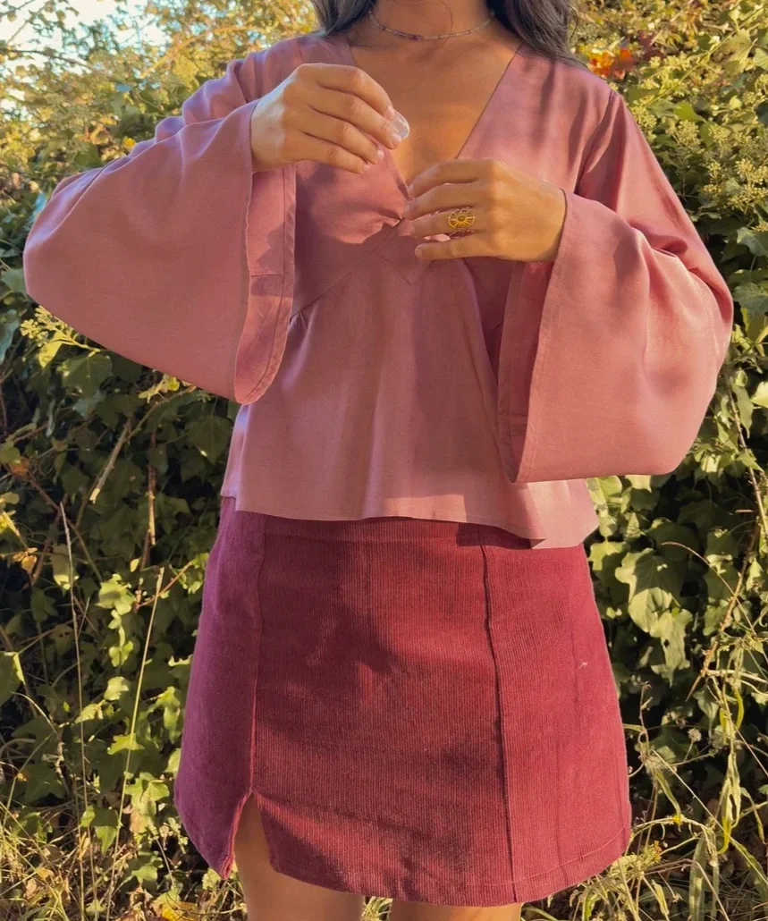 Mujer en la naturaleza luciendo la blusa mística Devi en color violeta, destacando las amplias mangas acampanadas y el tejido teñido con plantas medicinales