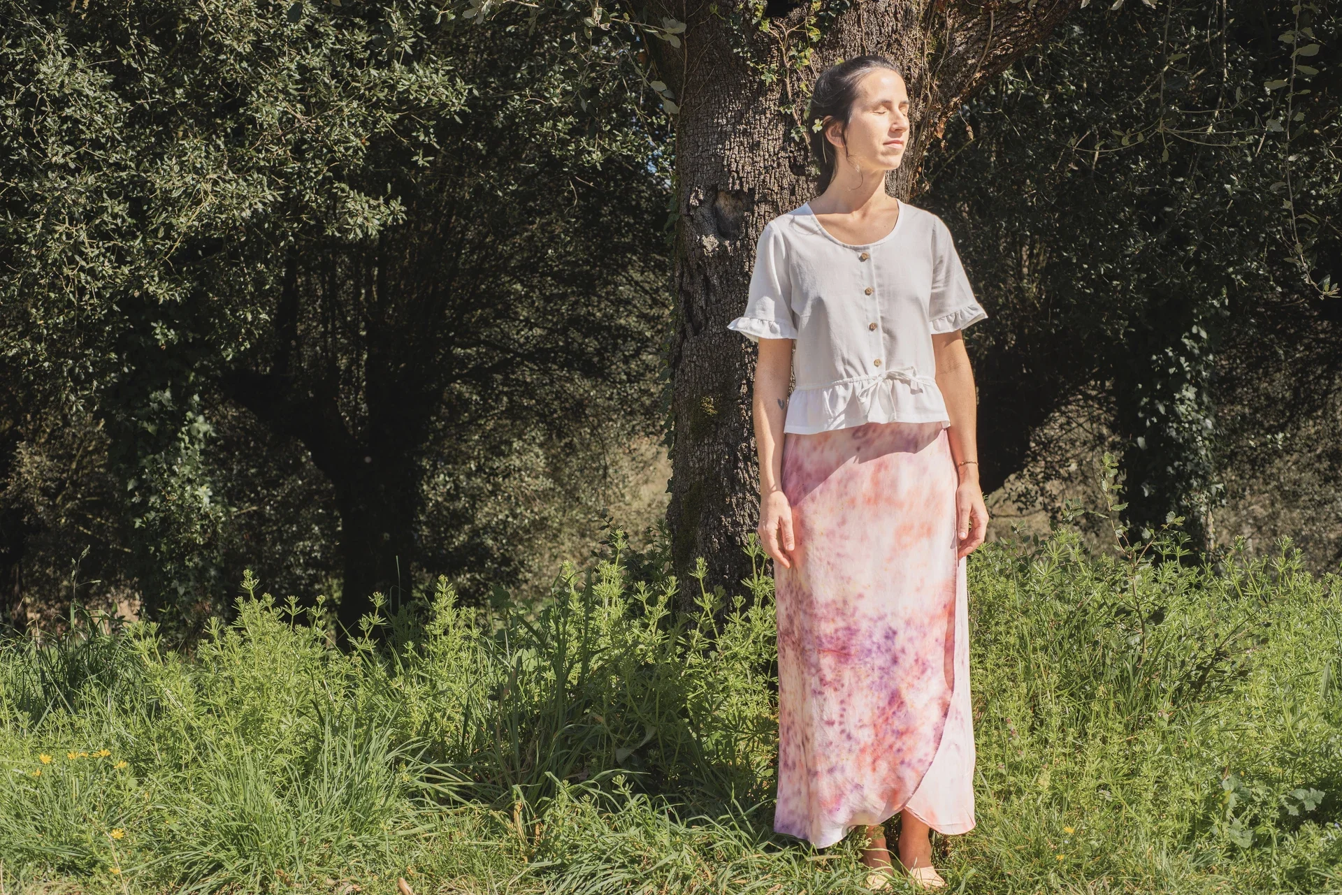 Mujer en la naturaleza vistiendo la falda pareo Prema. Prenda única de diseño artesanal con estampado de flores elaborado a mano en el taller.