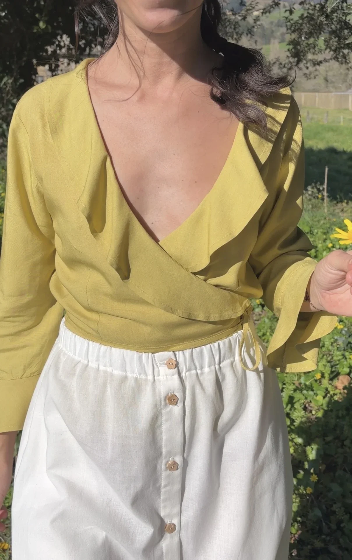 Mujer vistiendo la Blusa Agni cruzada de color verde pistacho, confeccionada en fibra de loto natural con detalles de volantes en las mangas