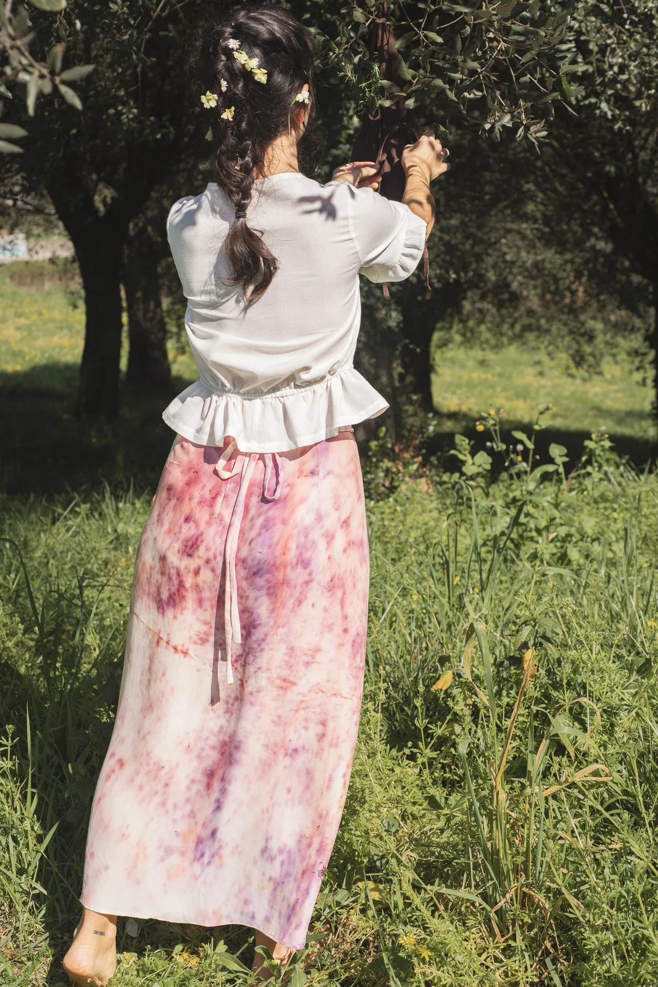Mujer en la naturaleza vistiendo la falda pareo Prema. Prenda única de diseño artesanal con estampado de flores elaborado a mano en el taller.