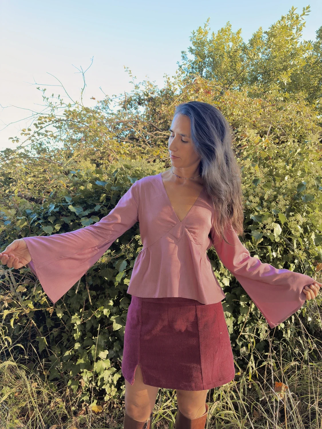 Mujer en la naturaleza luciendo la blusa mística Devi en color violeta, destacando las amplias mangas acampanadas y el tejido teñido con plantas medicinales