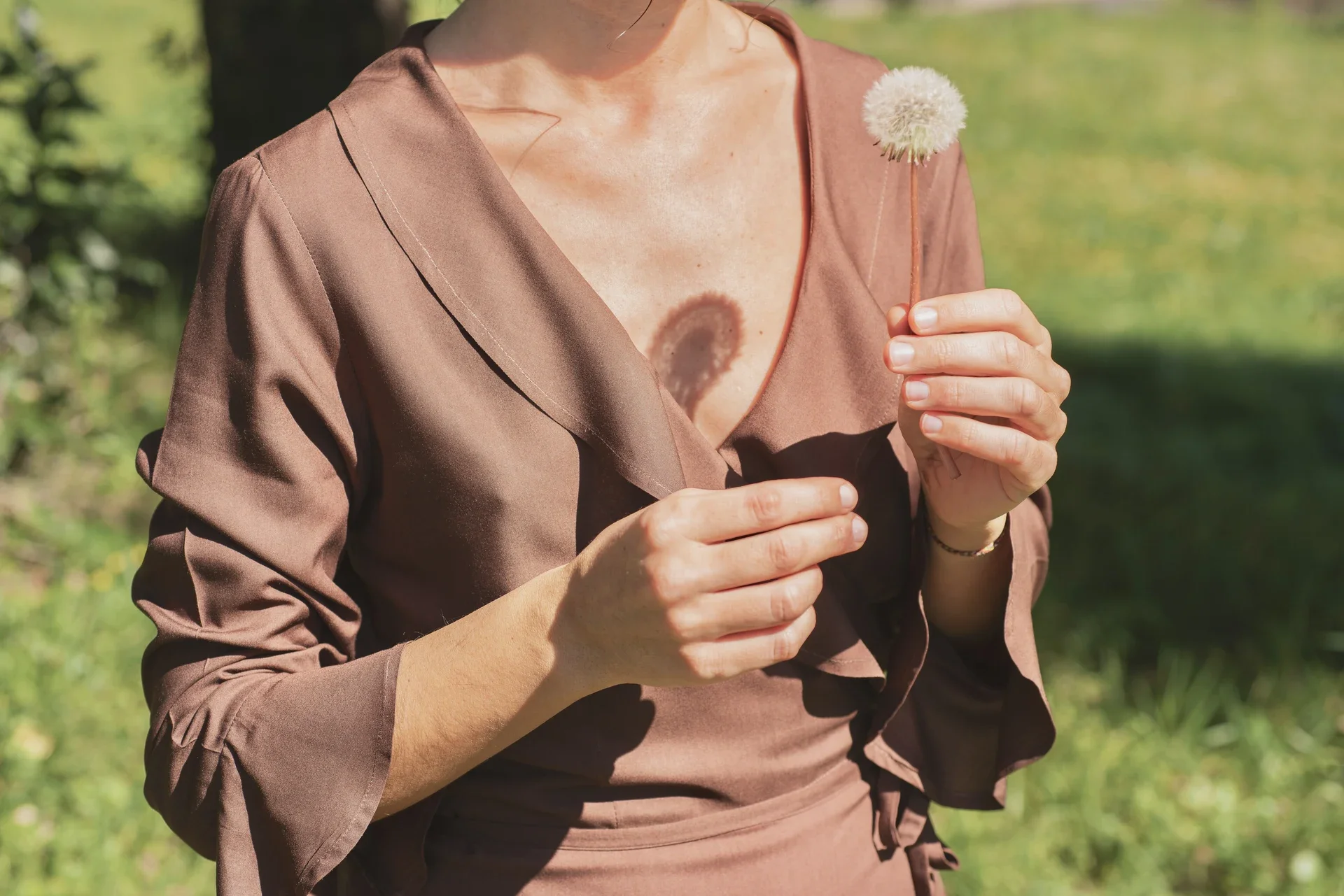 Mujer paseando por el campo vistiendo el vestido cruzado Agni en color marrón. Confeccionado en fibra de loto, alternativa vegana a la seda, y teñido con piel de granada y catechu