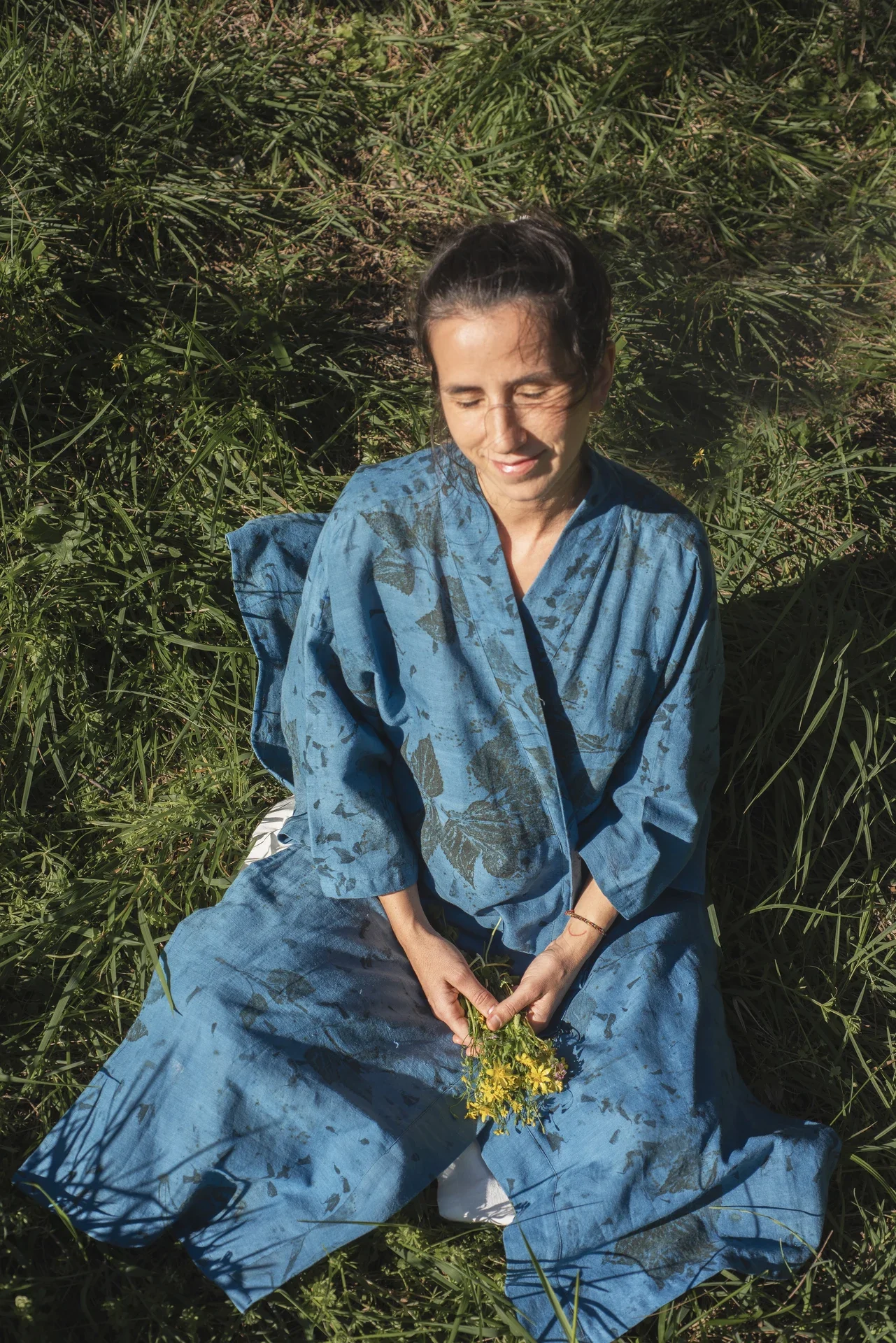 Mujer llevando un kimono azul teñido con índigo natural y estampación botánica en la naturaleza.