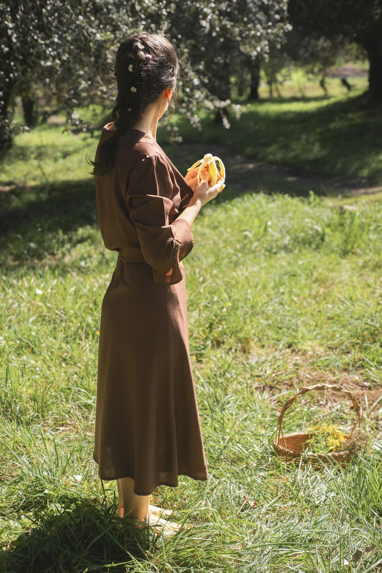 Mujer paseando por el campo vistiendo el vestido cruzado Agni en color marrón. Confeccionado en fibra de loto, alternativa vegana a la seda, y teñido con piel de granada y catechu