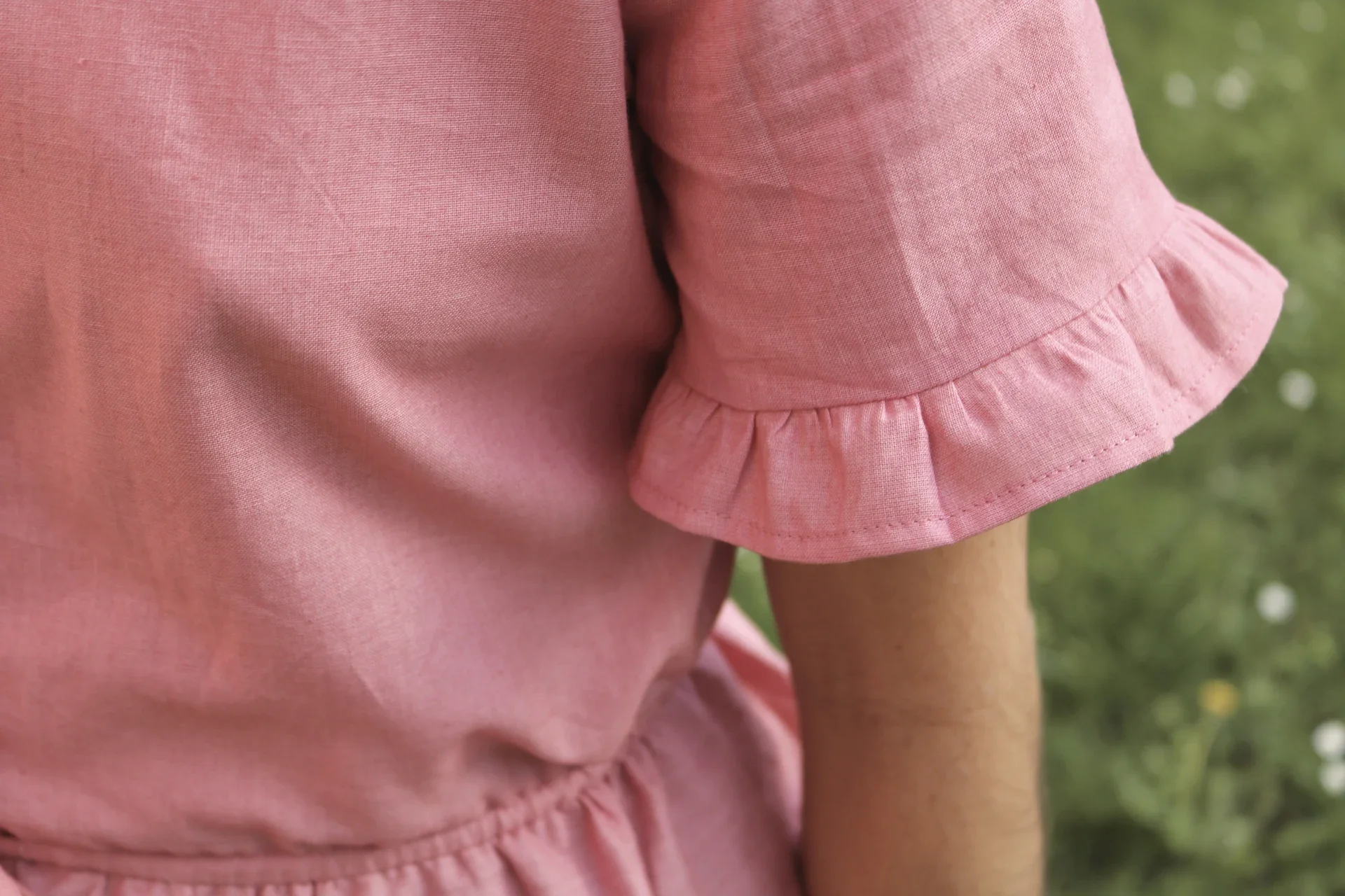 Blusa Aura de algodón orgánico en rosa de Madder Root, destacando sus botones de madera en forma de flor y el lazo ajustable en la cintura.